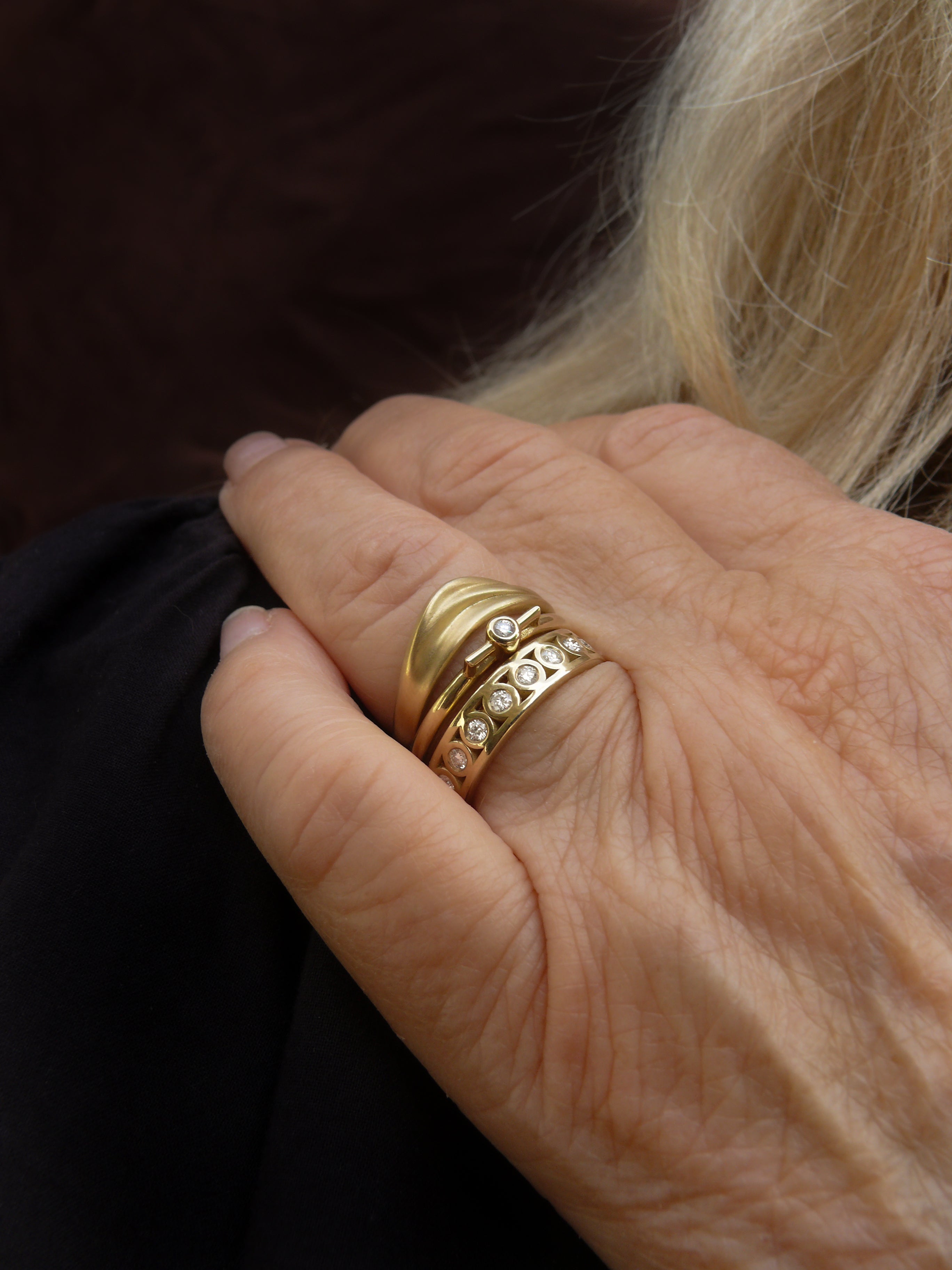 Close-up of a hand wearing a gold curved dune ring and diamond vessel ring with a diamond eternity band.