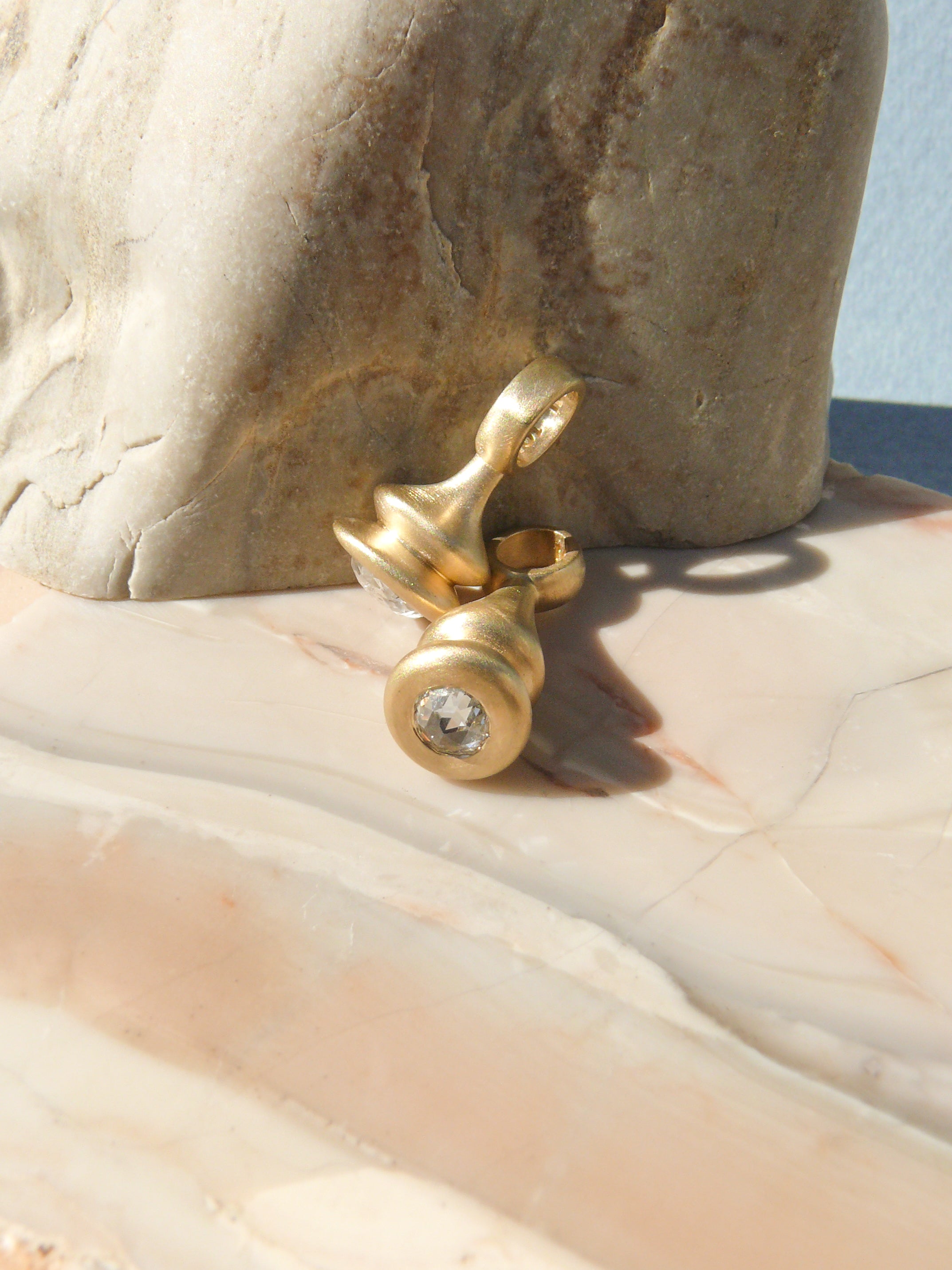 two gold diamond rose cut pendulum charms leaning on a rough rock
