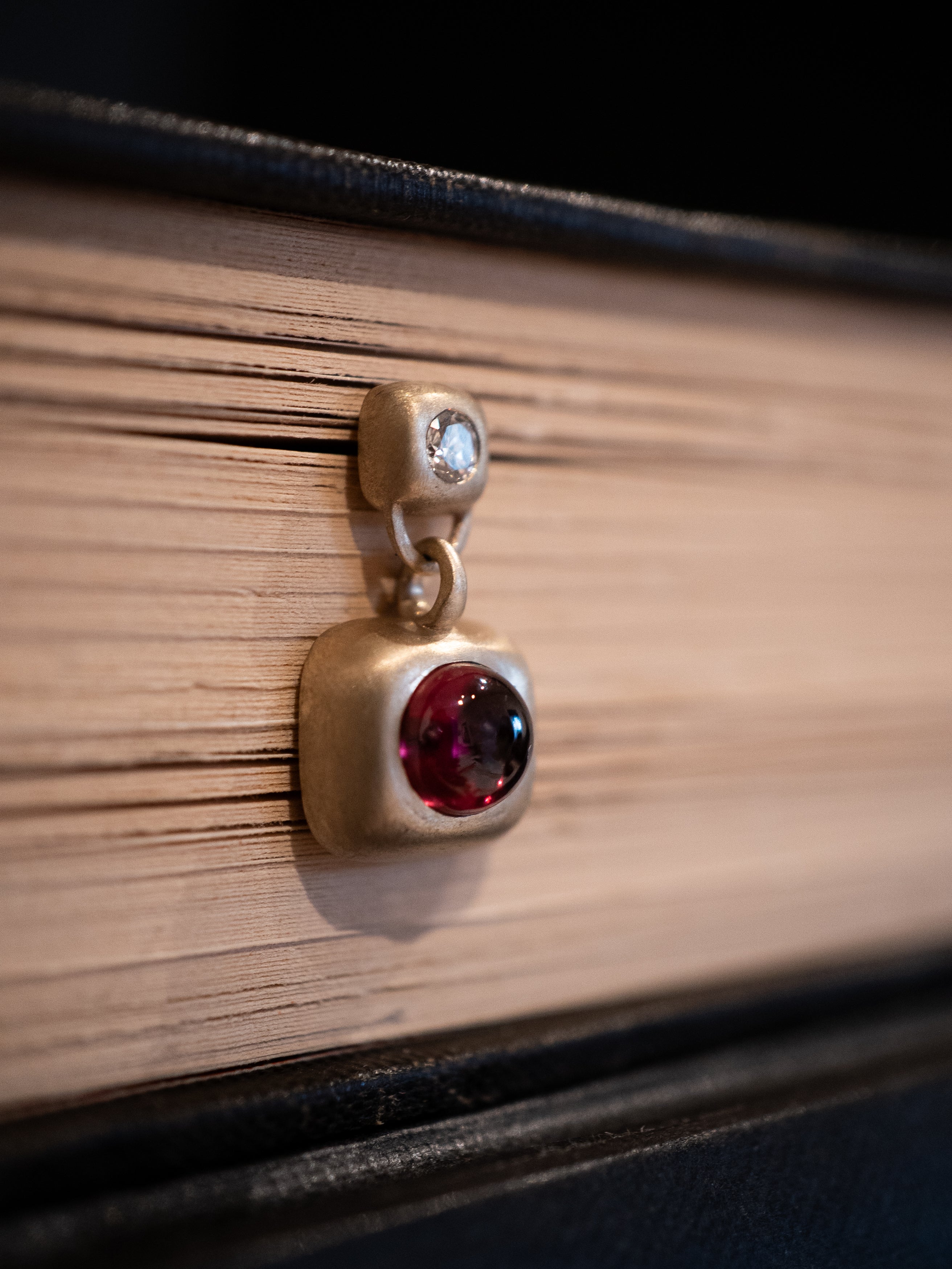 Gold earring with a red garnet and white diamonds on a book surface