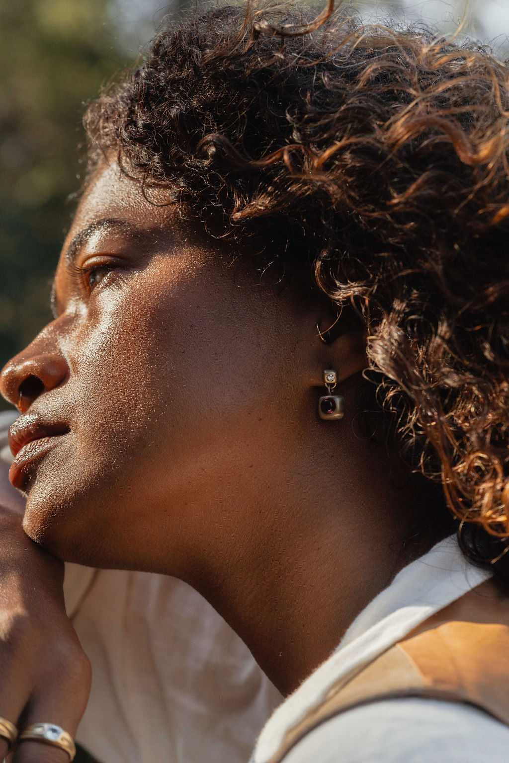 Close-up of a person with curly hair wearing trove drop earrings with garnet and diamonds and a white top.
