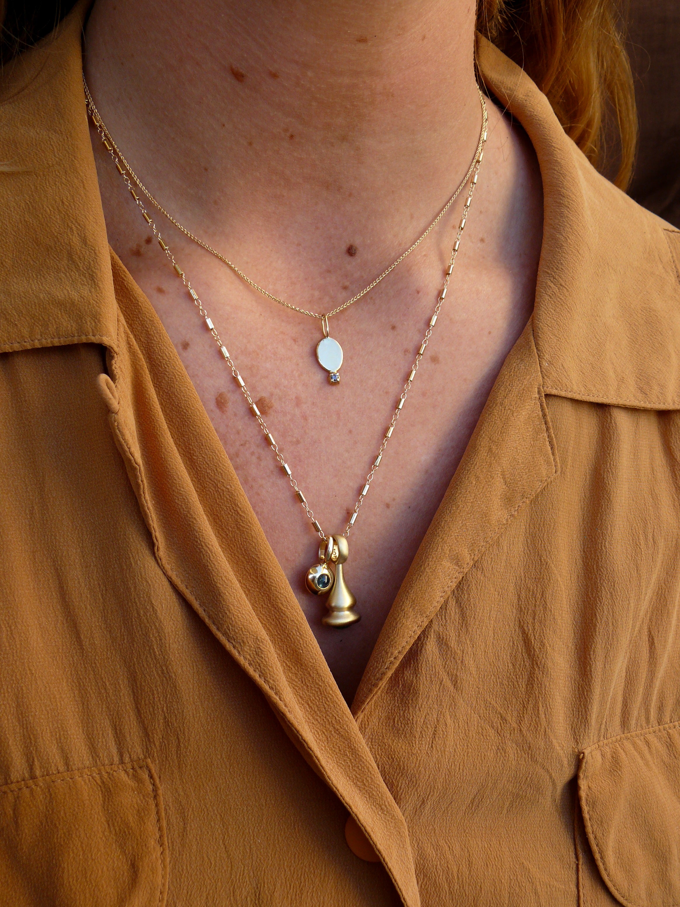 Gold sapphire and diamond reflection charm on model with stellar bar chain and blossom medallion