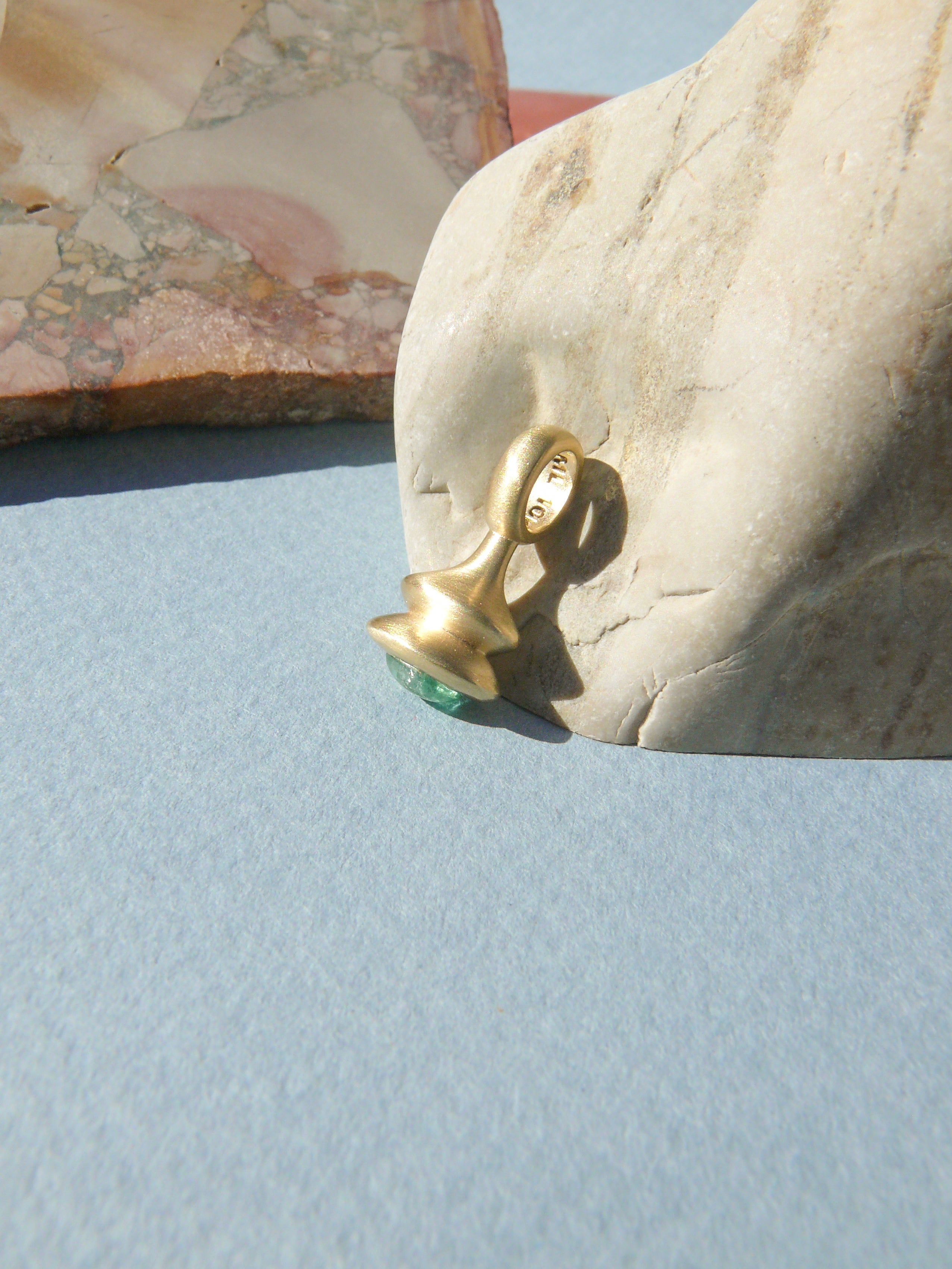 Gold pendulum charm with a green beryl on a rough rock background