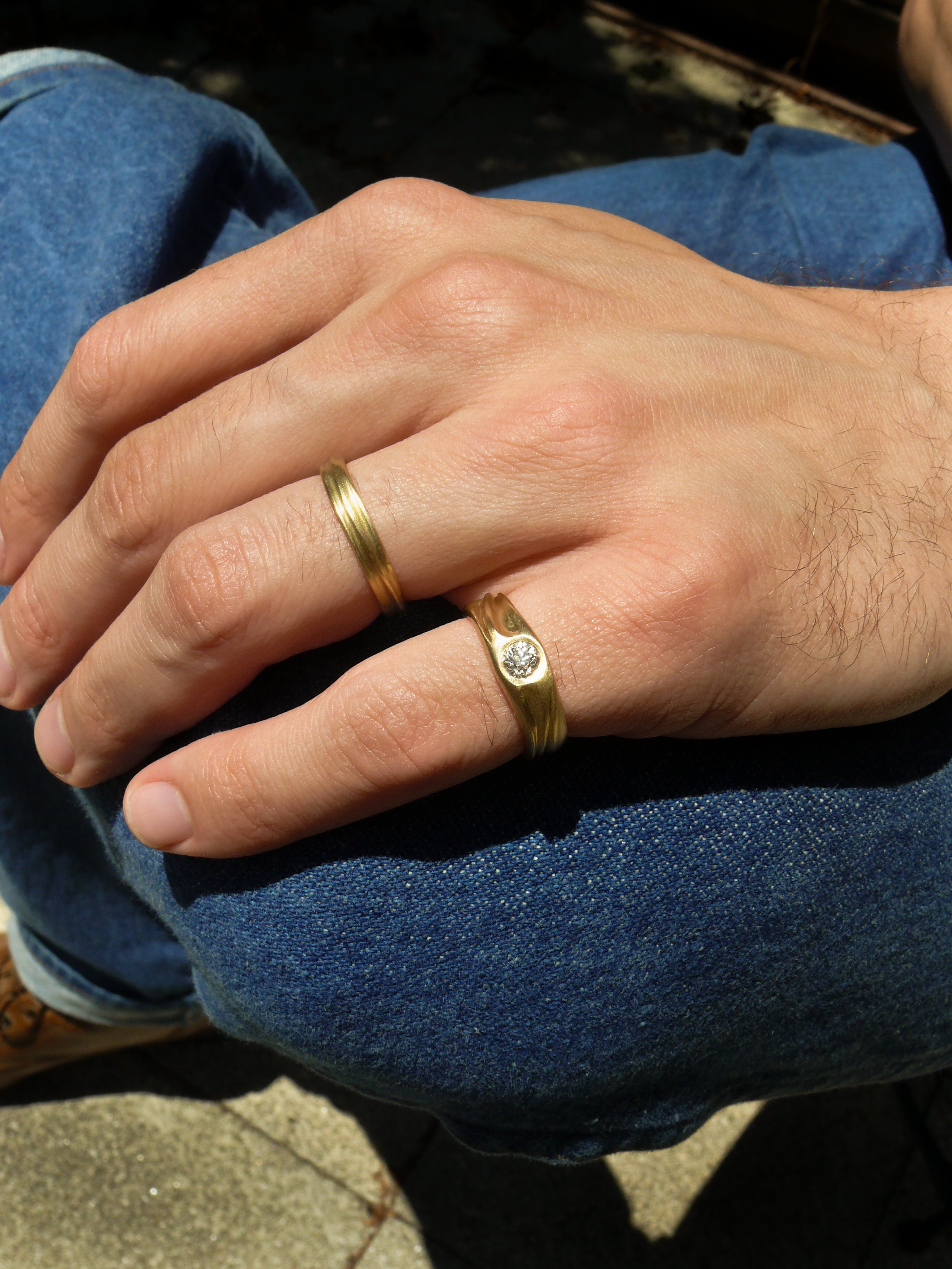 Close-up of a hand wearing old european cut diamond pinky ring and narriw dune ring with blue jeans in the background