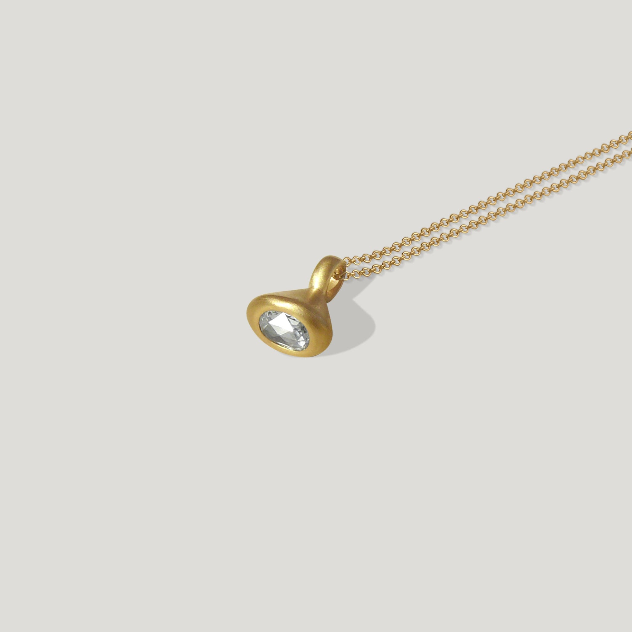 A gold pendulum charm with a rose cut diamond set in a gold mount, suspended from a gold chain.
