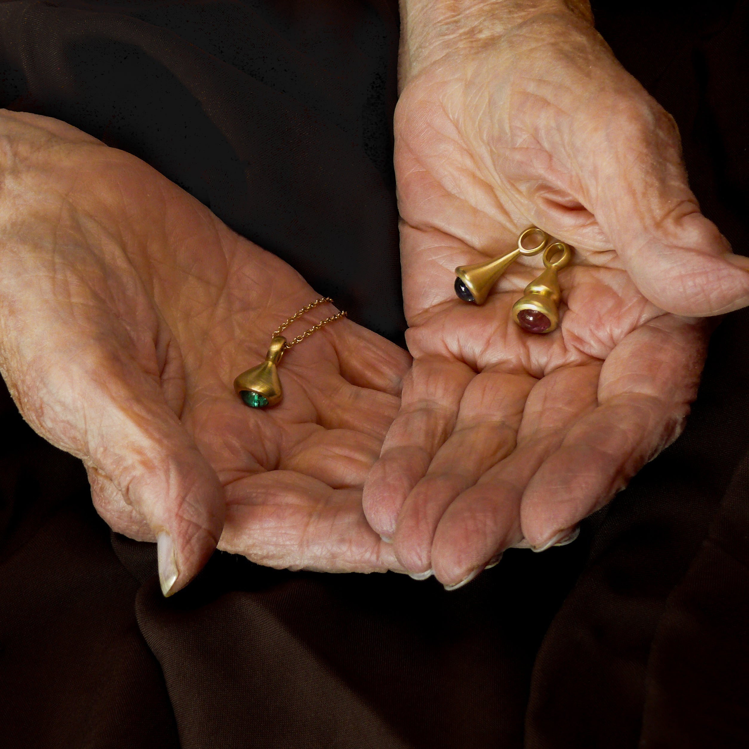 gold pendulum charms with teal tourmaline, blue sapphire, and pink tourmaline in grandma's hands