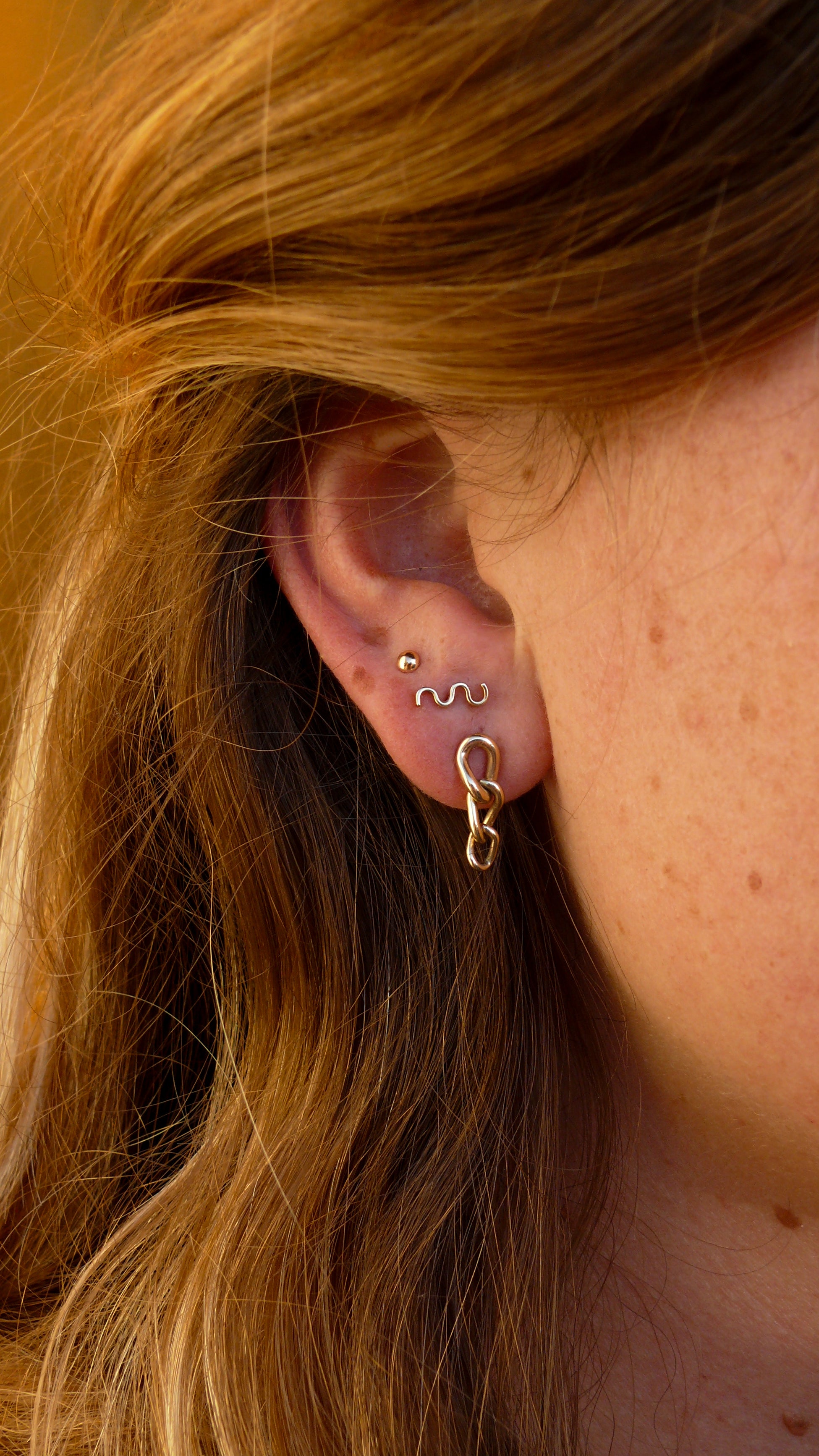 Gold short curb chain earrings stacked on ear with gold breeze and grain studs