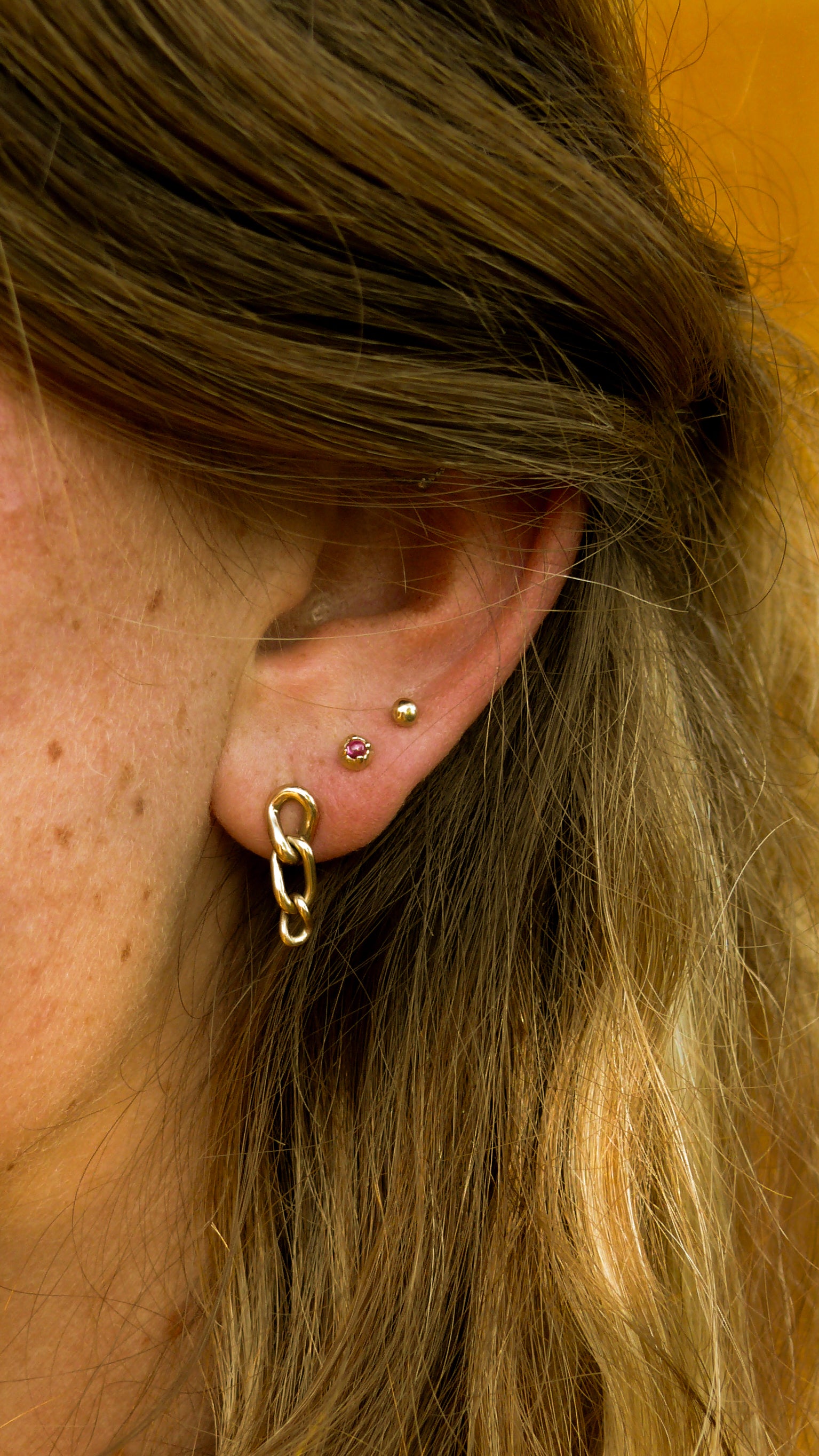Gols short artisan curb chain earrings stacked on an ear with gold ruby and grain stud