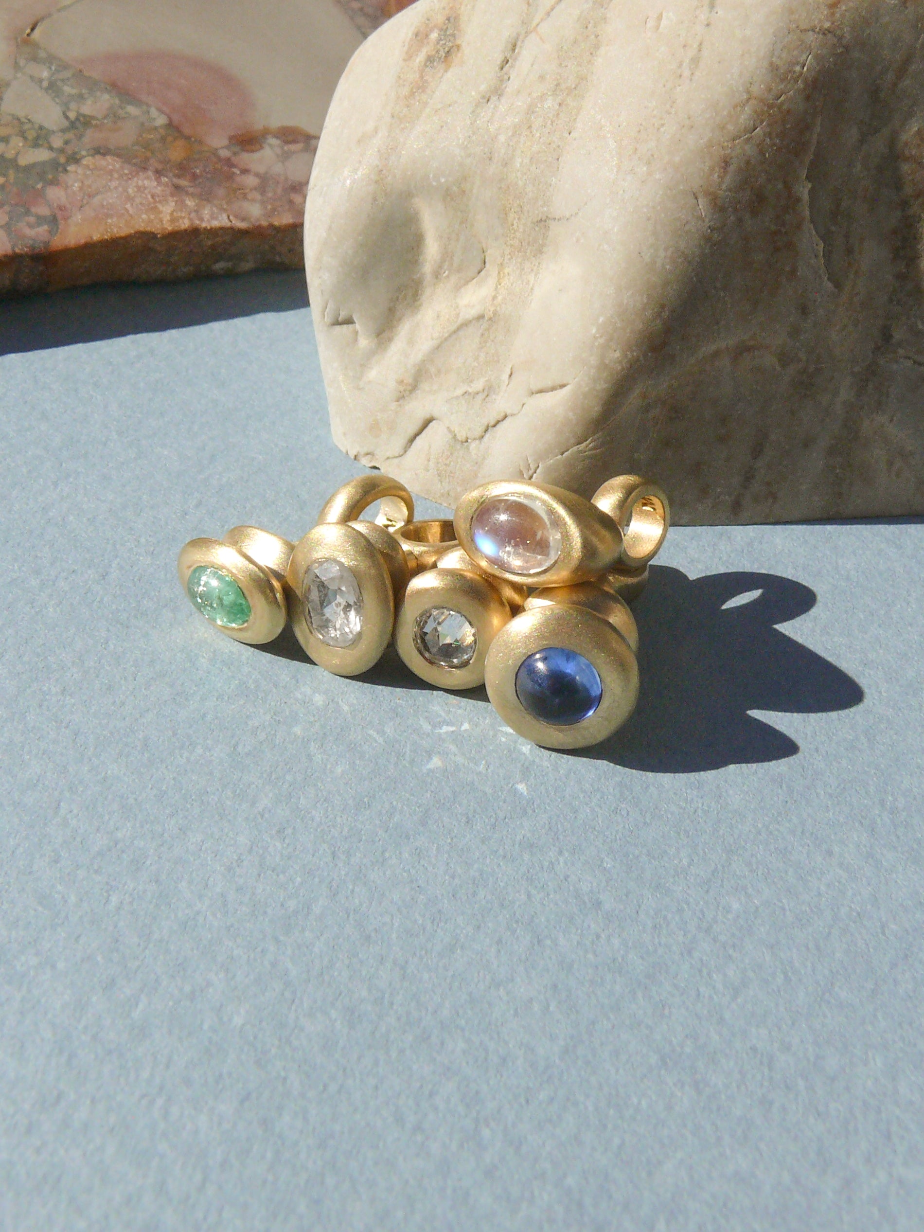 gold pendulum charms with bright gemstones and diamonds on rough rock background
