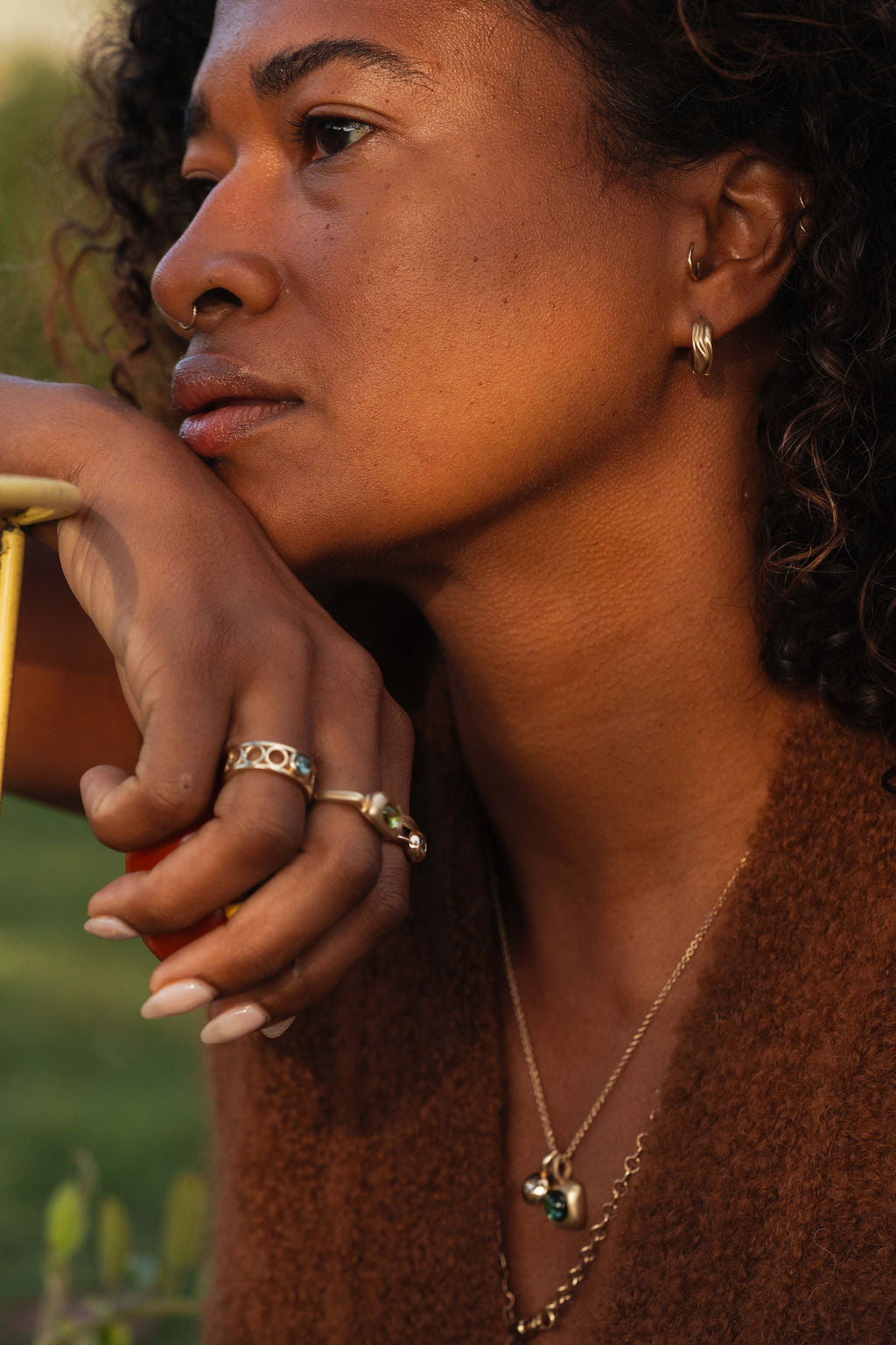 Woman wearing gold huggie hoop earrings and rings with a blurred natural background