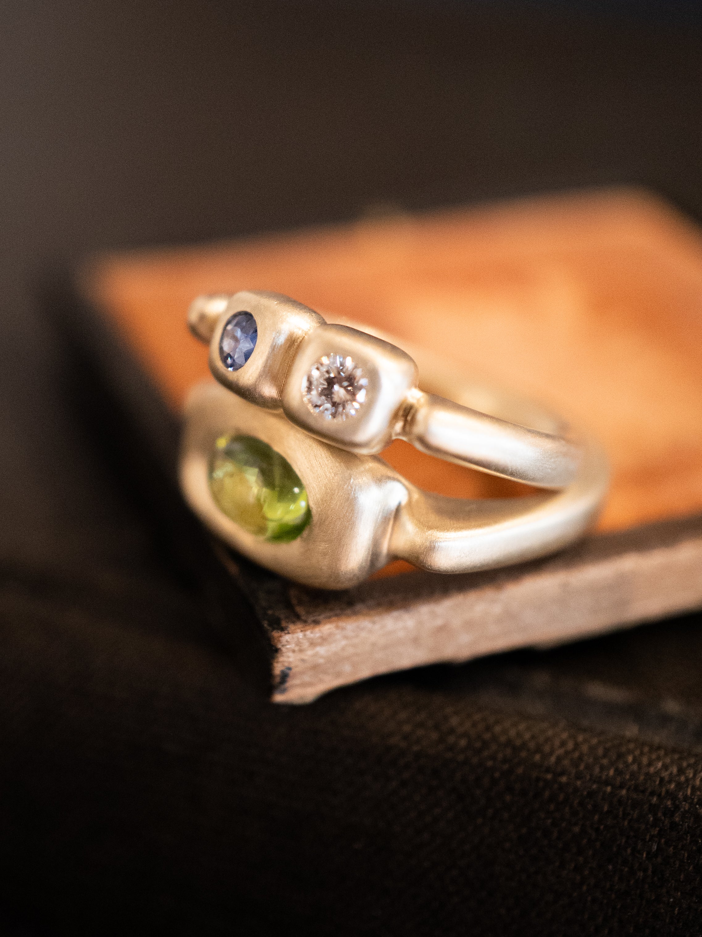 Gold ring with diamonds, sapphires, and peridot on a dark surface