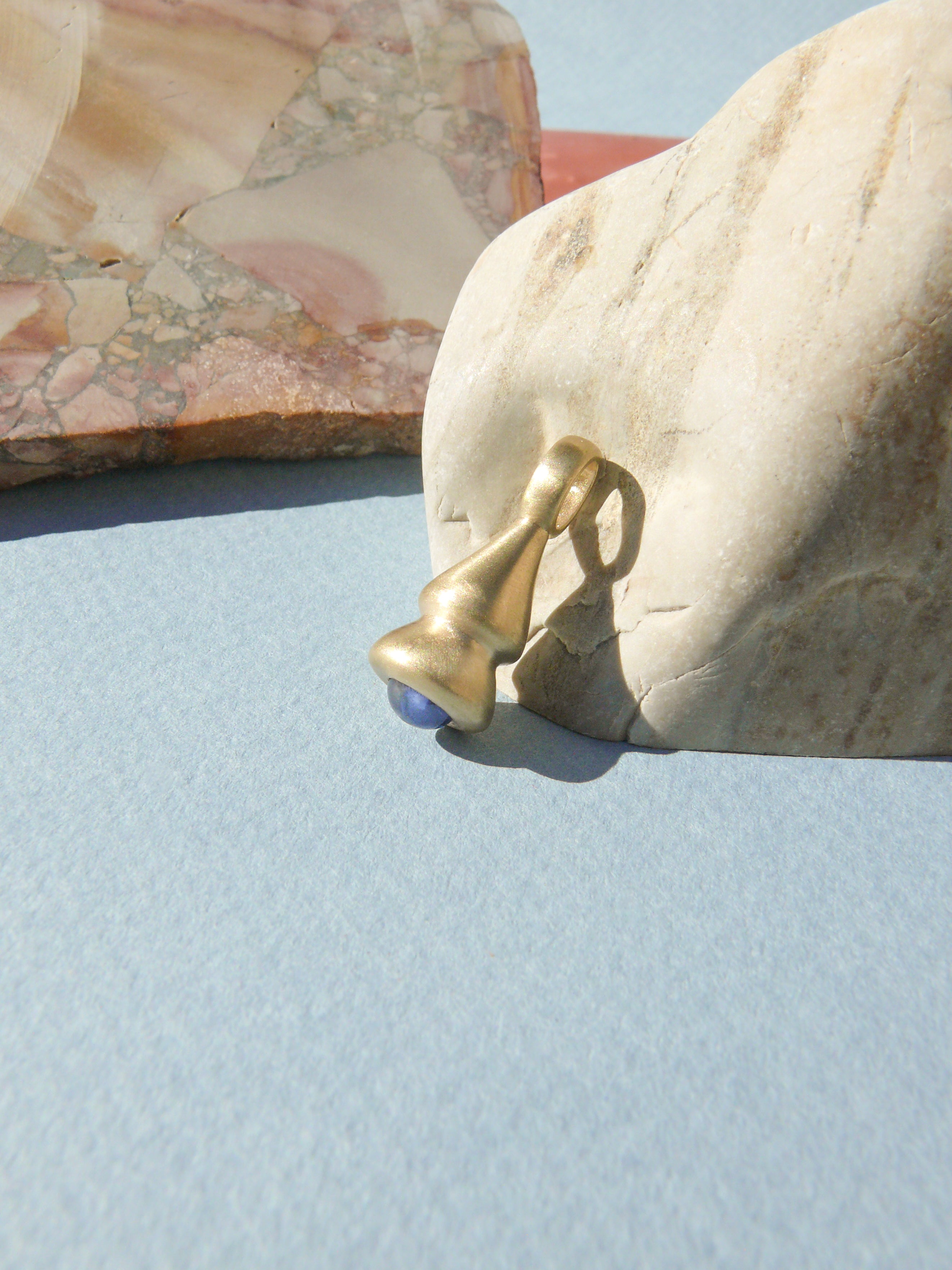 blue sapphire pendulum charm no. 1 on rough rock background