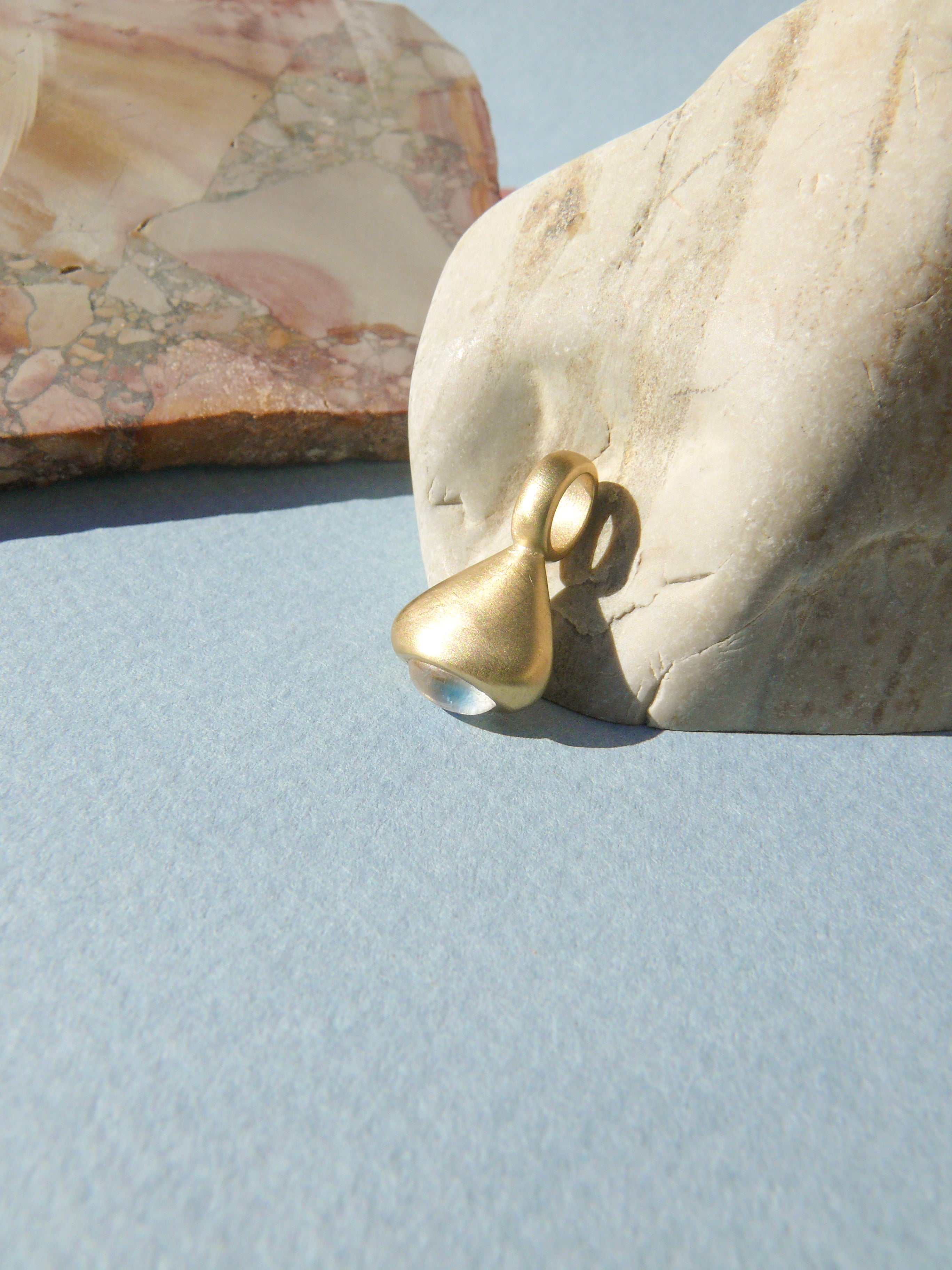 gold moonstone pendulum charm no. 3 leaning on rock