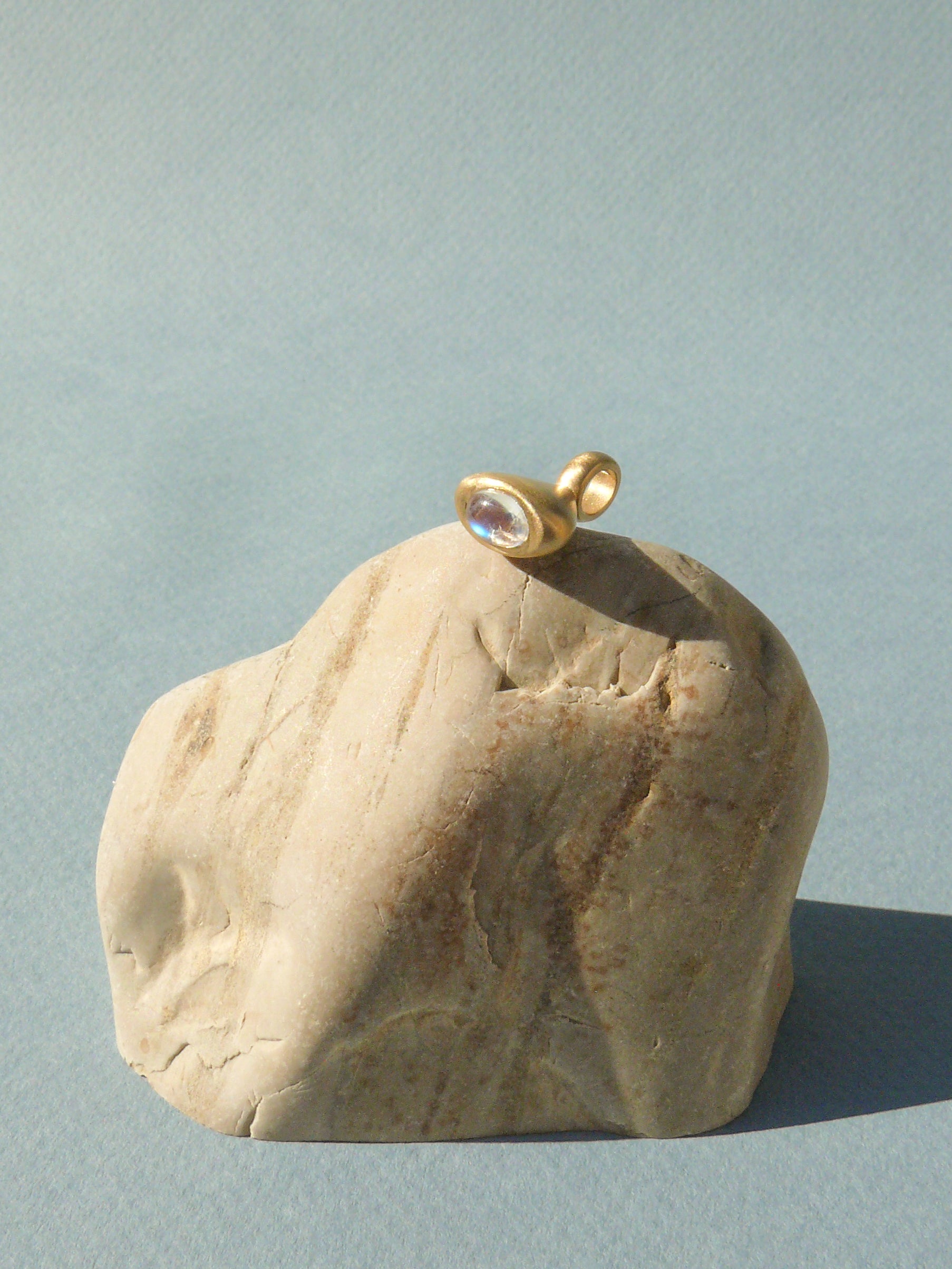 gold moonstone pendulum charm no. 3 on rough rock