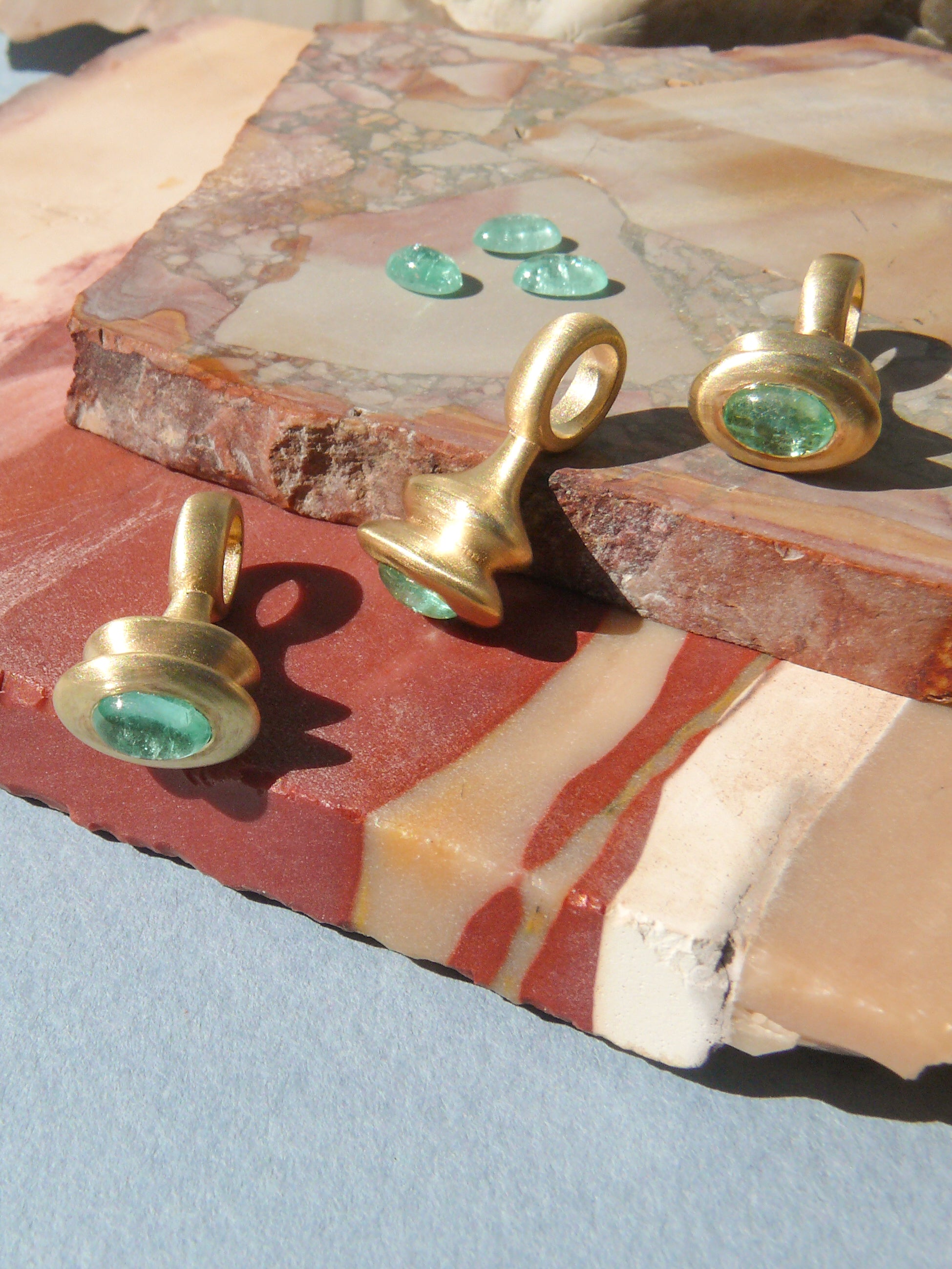 Gold pendulum charm with a green beryl on a rough jasper slab background