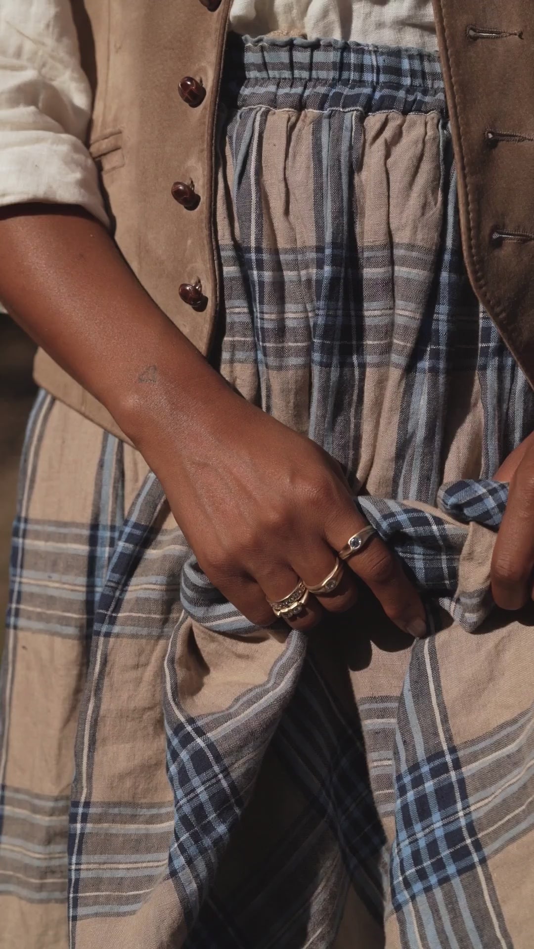Model wearing blue plaid skirt and white shirt and leather vest, wearing gold trove collection jewelry with gemstones