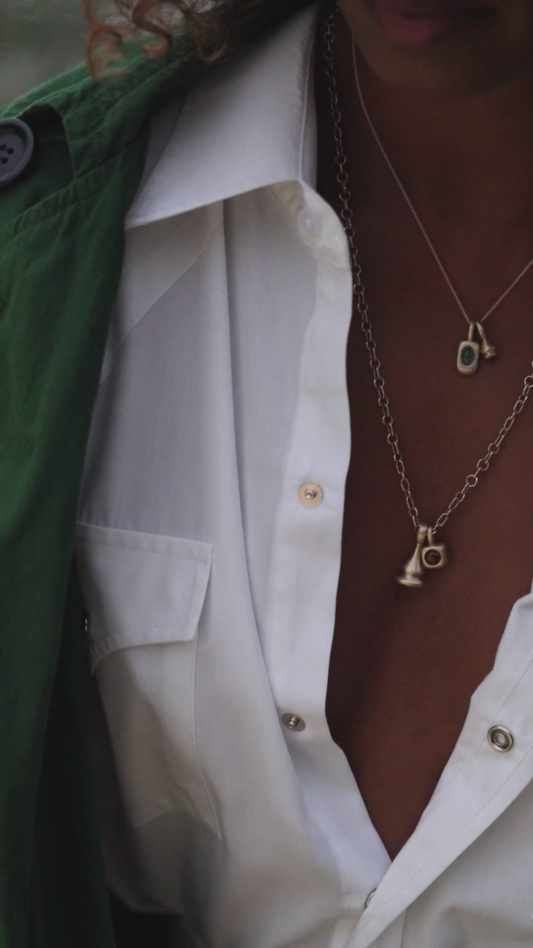 Model with curly hair wearing gold necklaces and charms with bright green tourmaline and red garnet