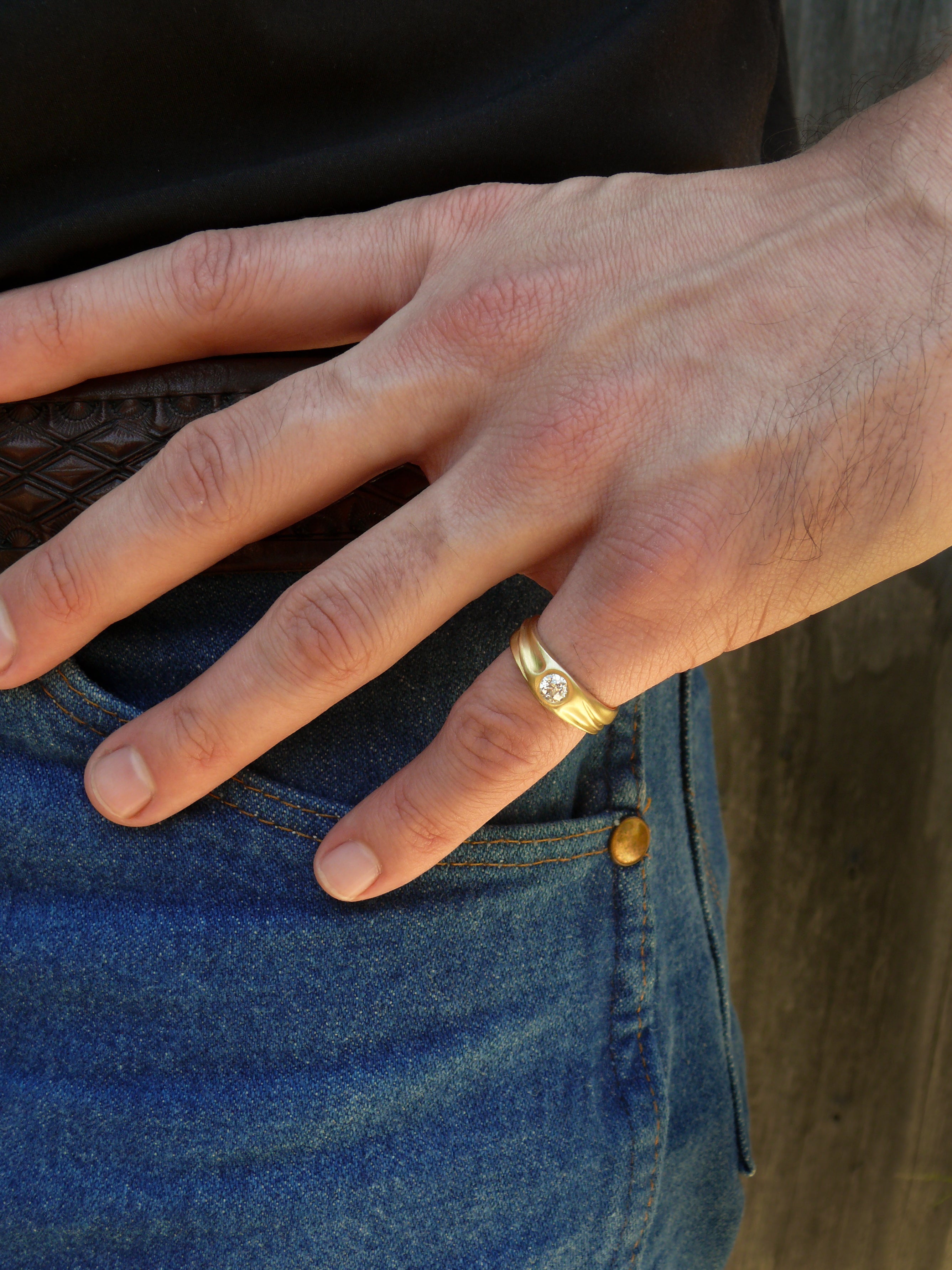 Hand wearing a gold diamond dune ring on a blue denim background