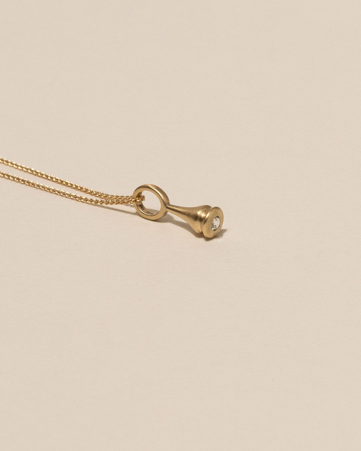 A gold pendant necklace featuring a teardrop-shaped pendant with a white Canadian rose cut diamond, displayed on a solid beige background.