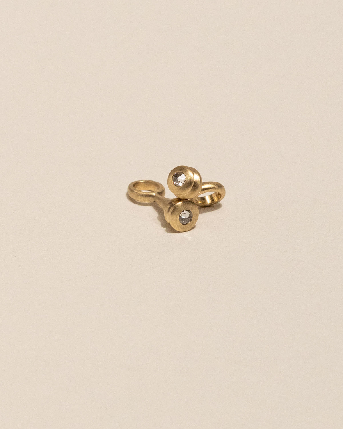 Two gold pendant necklaces featuring a teardrop-shaped pendant with a white Canadian rose cut diamond, displayed on a solid beige background.