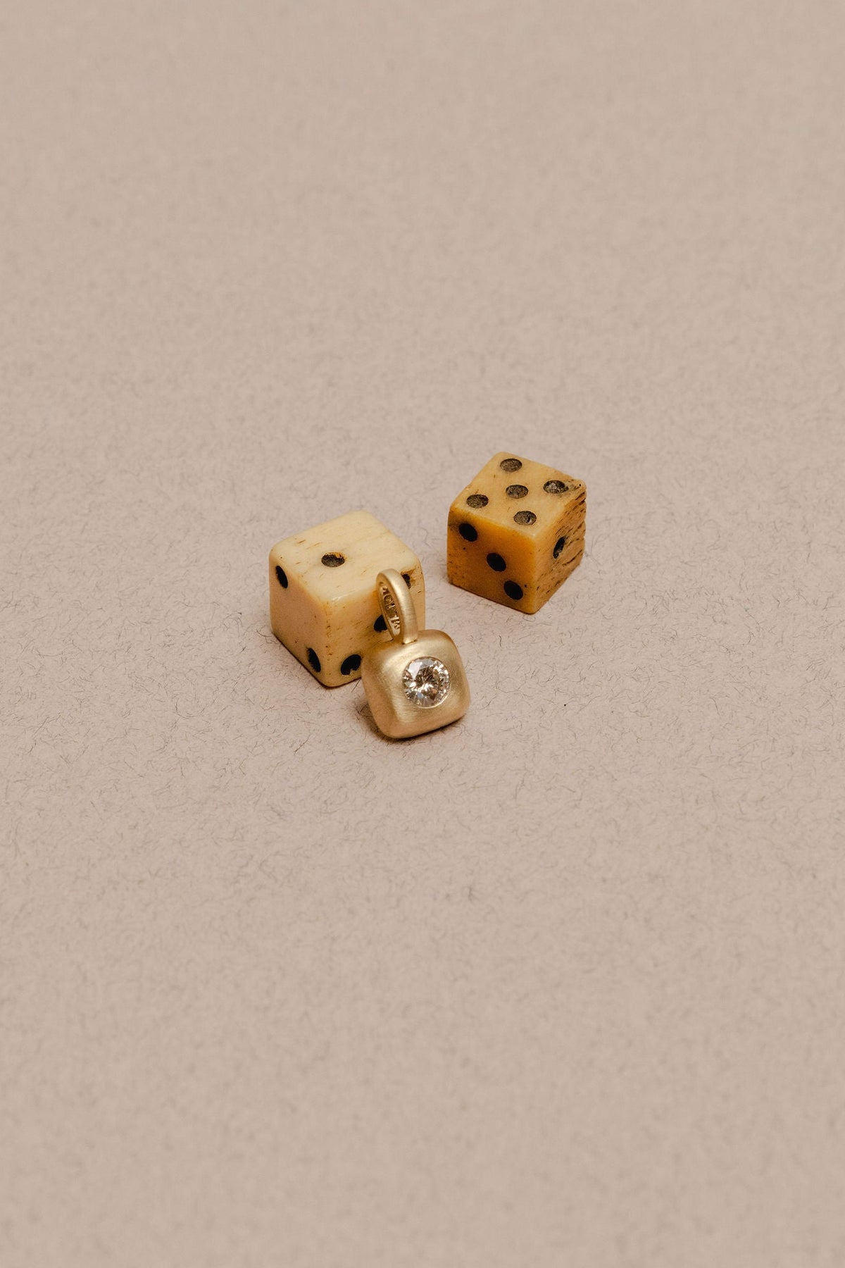 Classic diamond charm set in matte gold in a box form, photographed with vintage dice