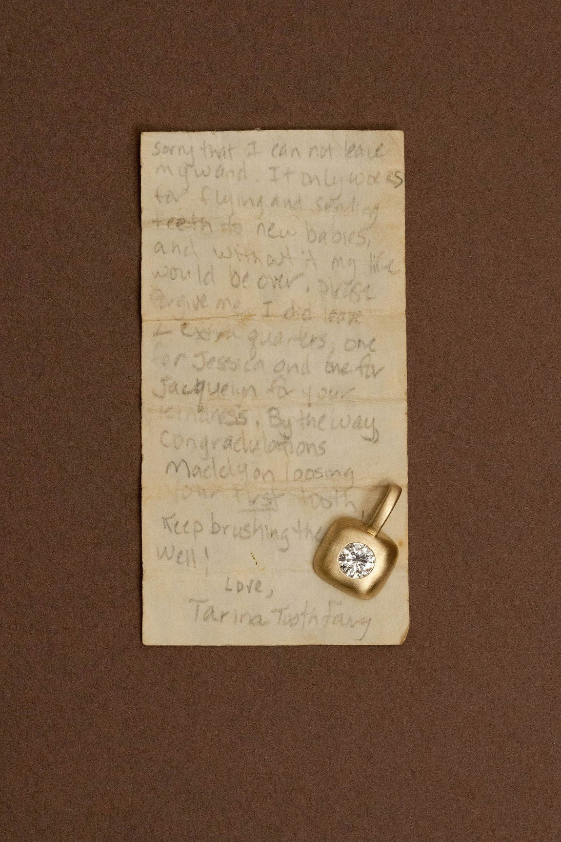 Classic diamond charm, flush set into matte gold shaped like a box, photographed on a handwritten note from the tooth fairy