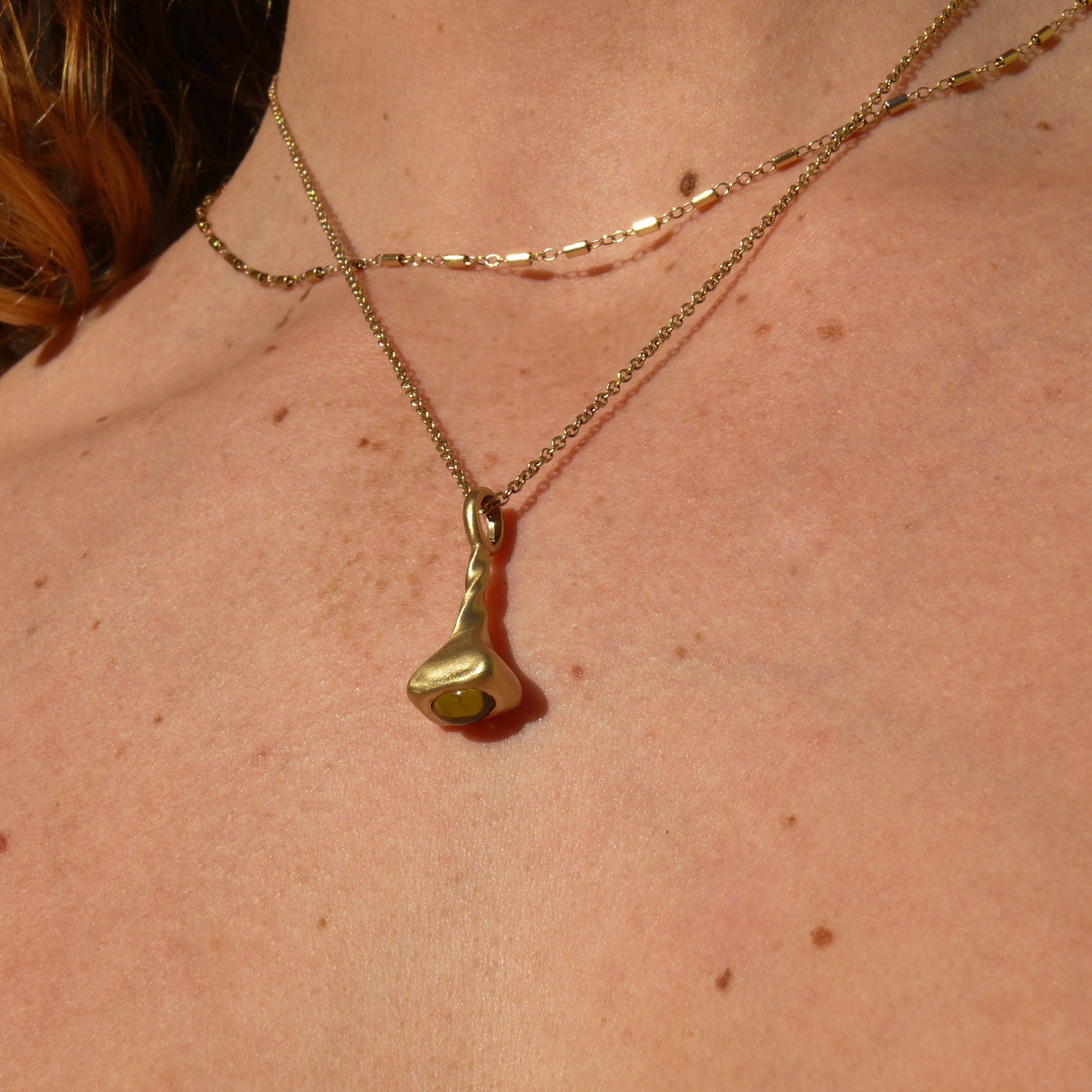 Neck with gold stellar bar chain and 1.5mm strand cable chain with peridot pendulum charm