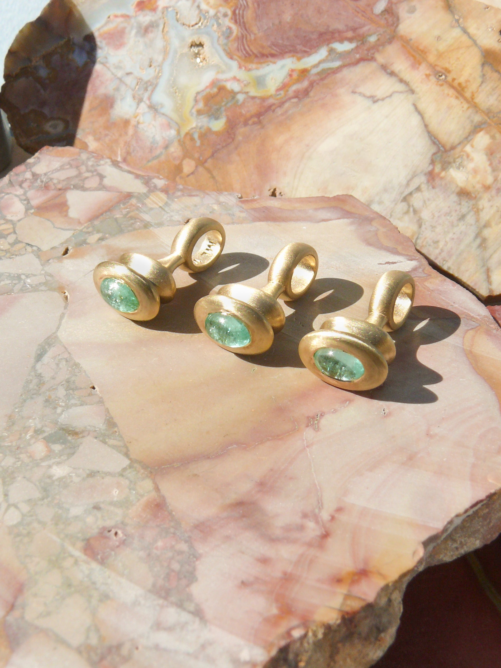 Gold pendulum charm with a green beryl on a rough jasper slab background