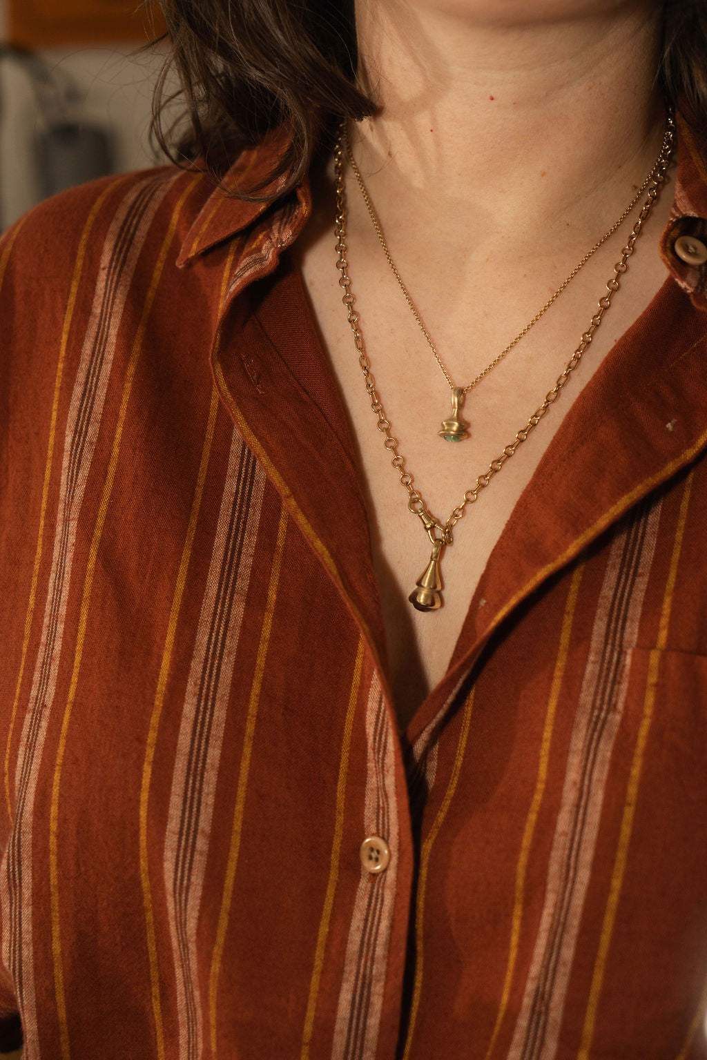 Green Beryl Pendulum charm No. 9 in gold on a neck with a person wearing a rust colored striped button down shirt