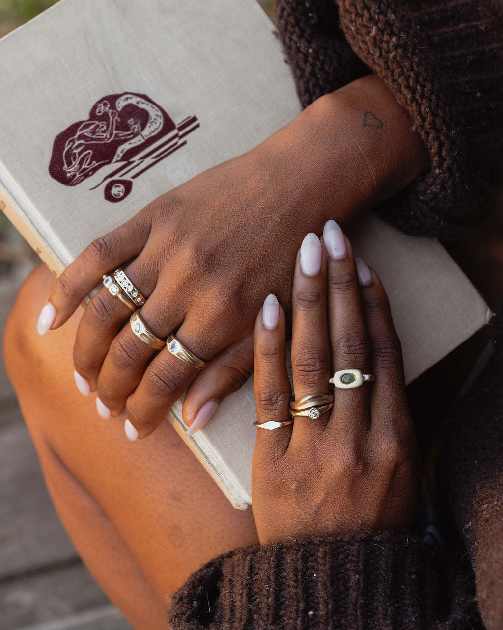 Person wearing multiple gold and gemstone rings on fingers, holding a book.