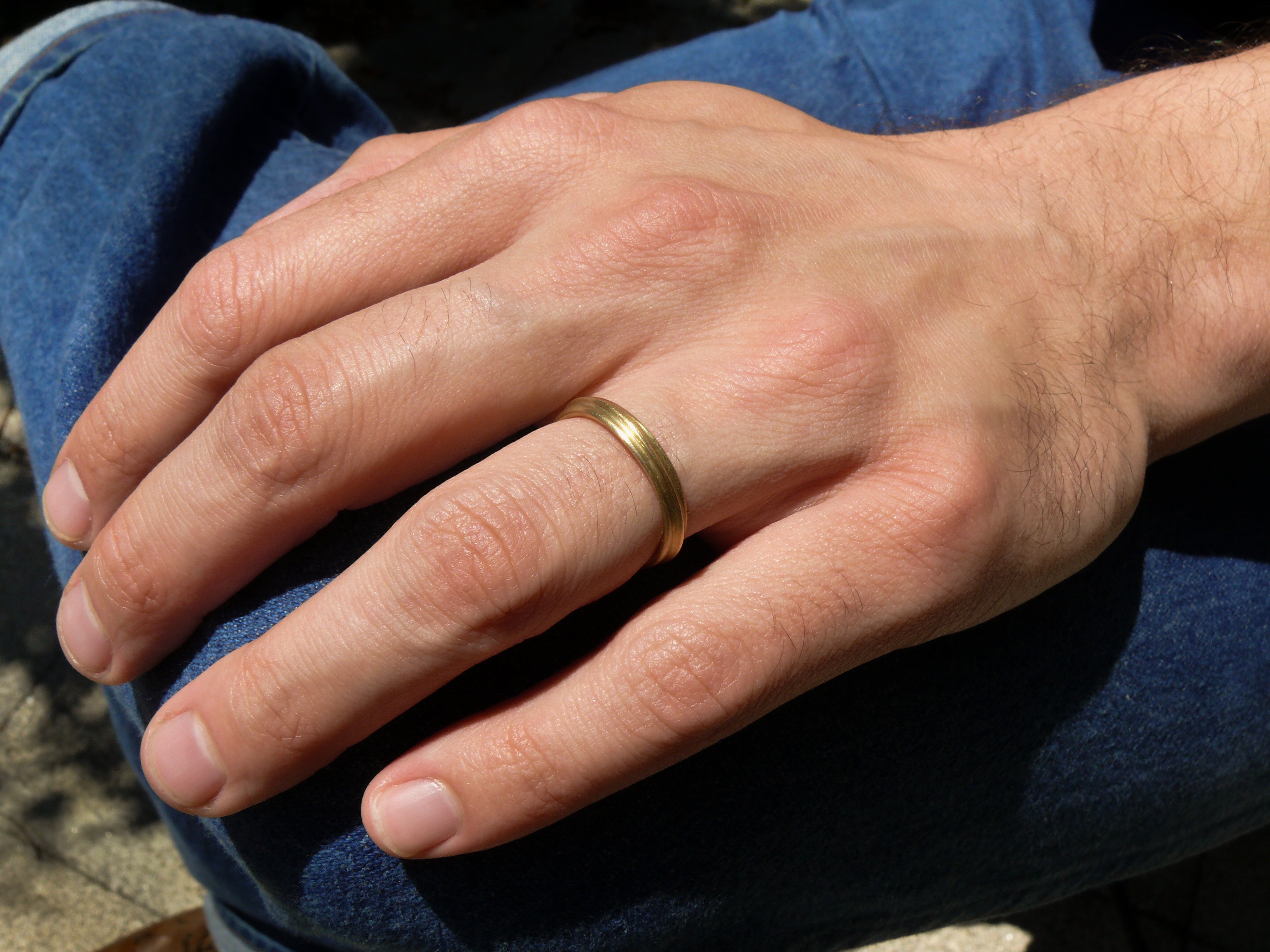 Hand wearing a gold narrow dune ring with denim jeans background