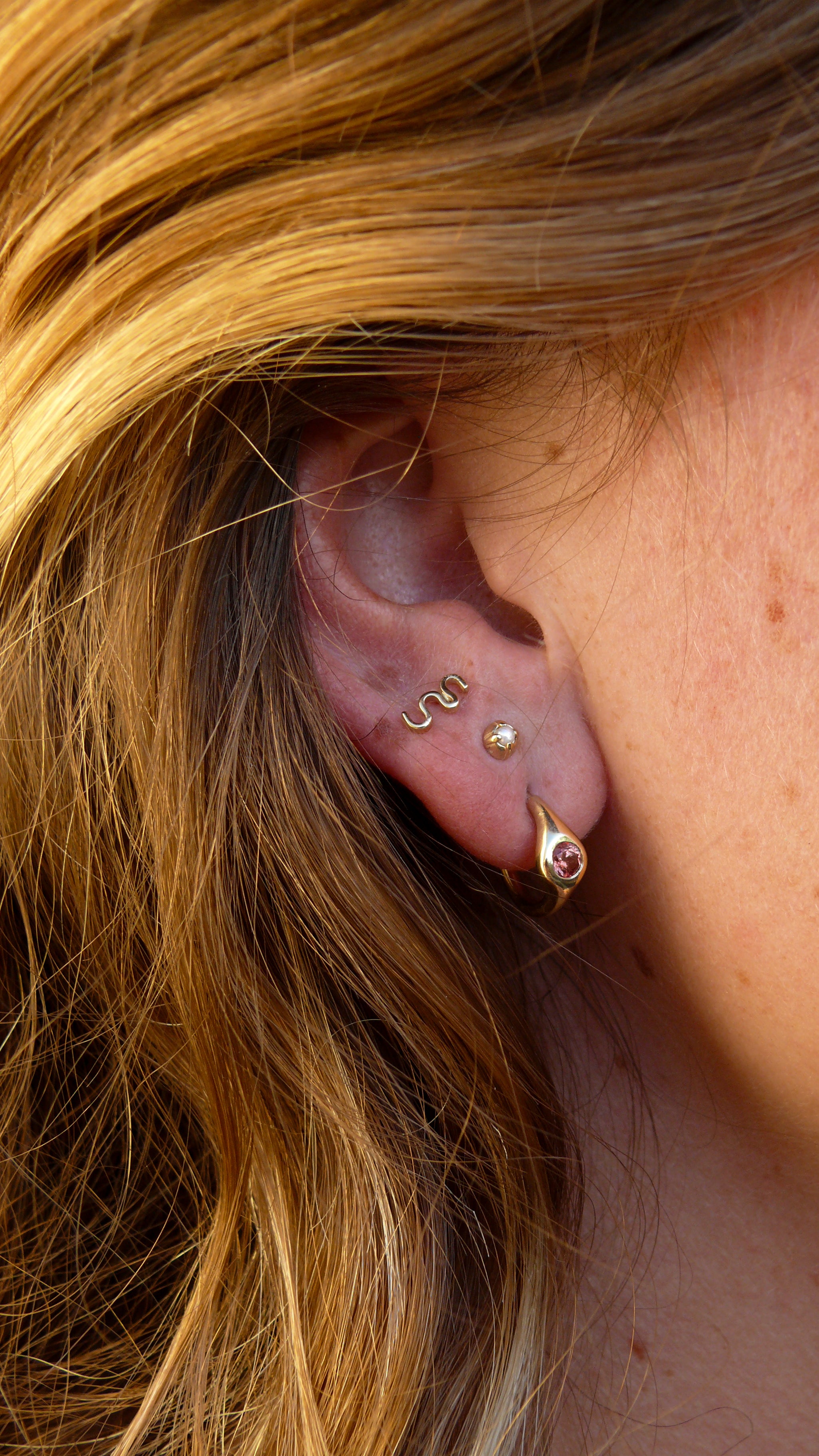 Padparadscha sapphire petite signet hoops stacked on an ear with gold pearl and flutter stud earring