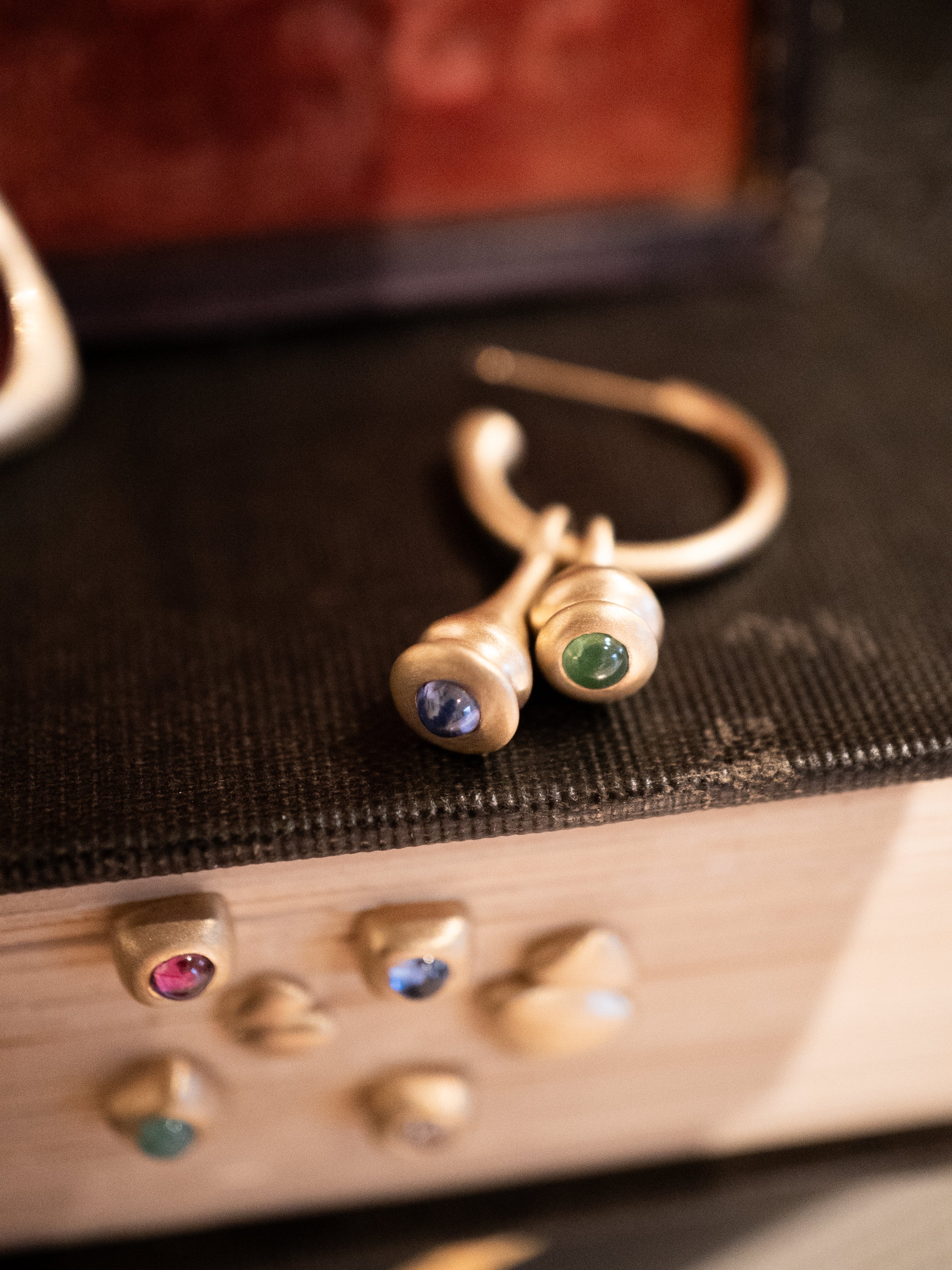 Gold pendulum charm hoop earrings with sapphires and emeralds on a textured surface