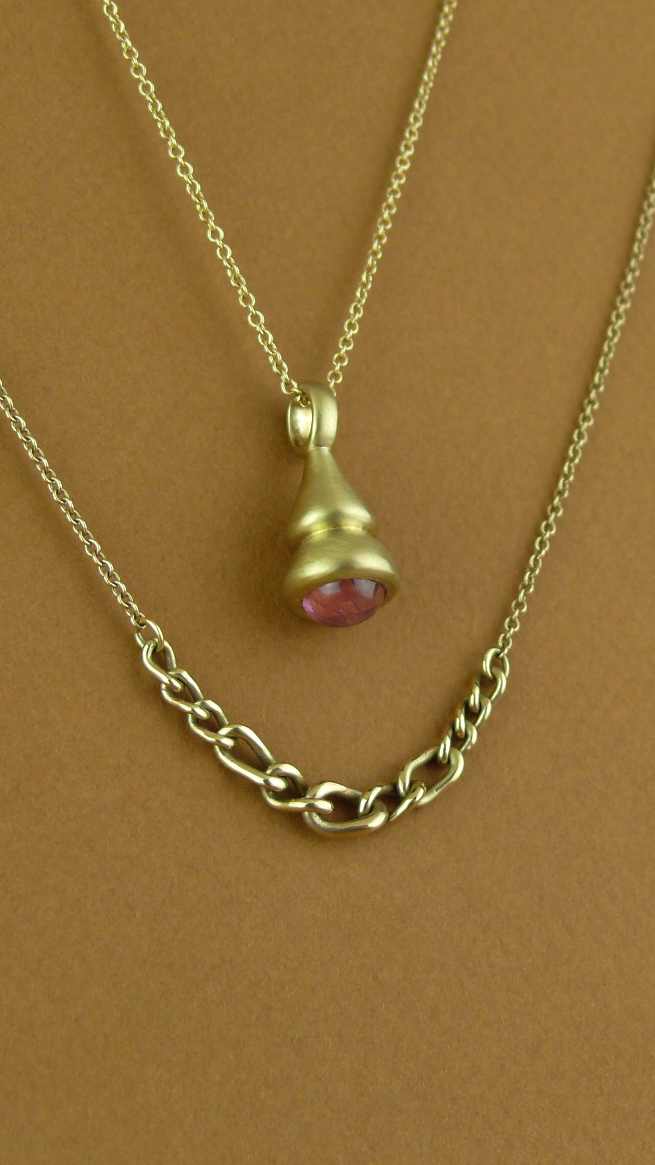pink tourmaline pendulum charm and graduated curb chain necklace on brown paper