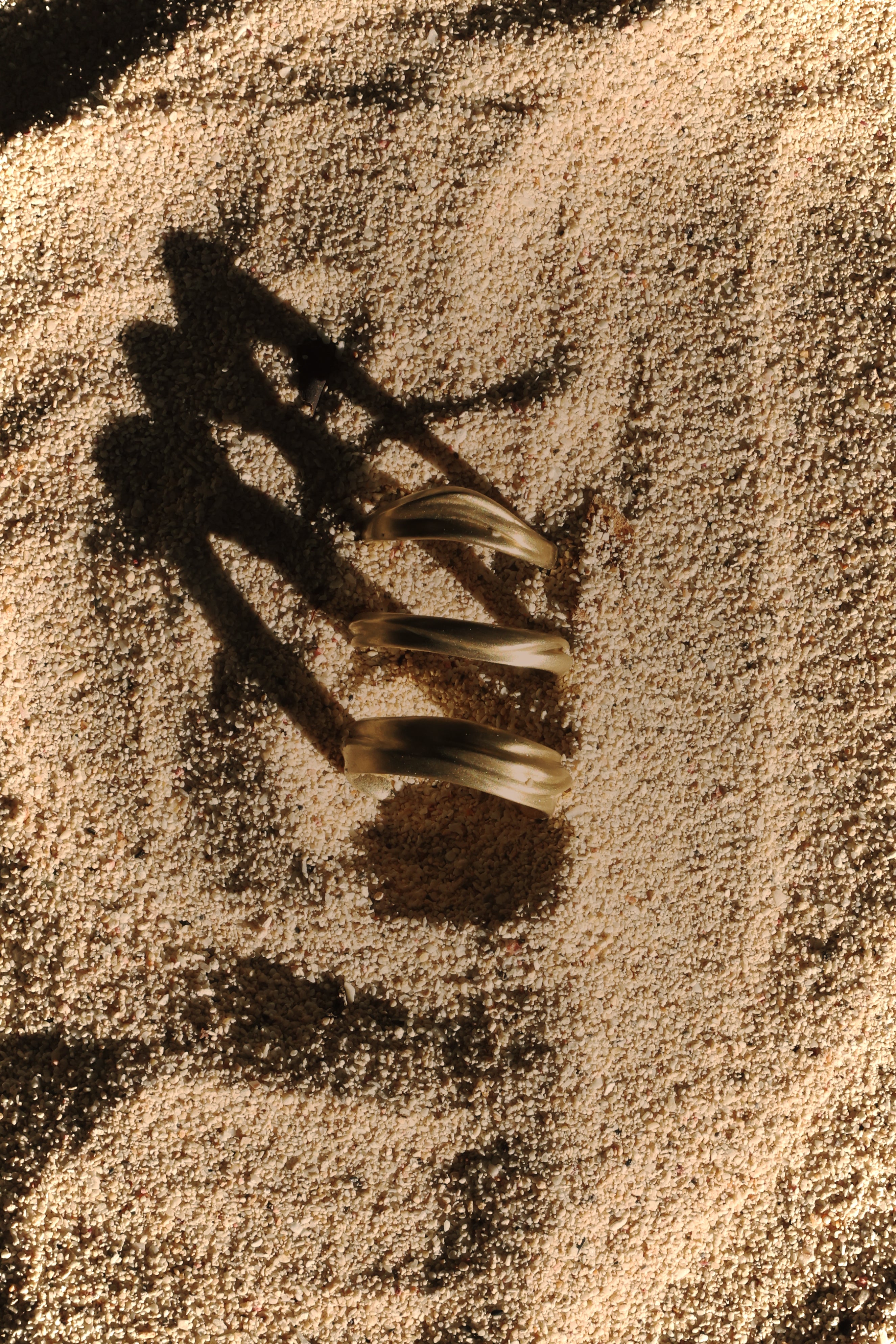 Organic gold dune rings on a sandy surface with visible shadow