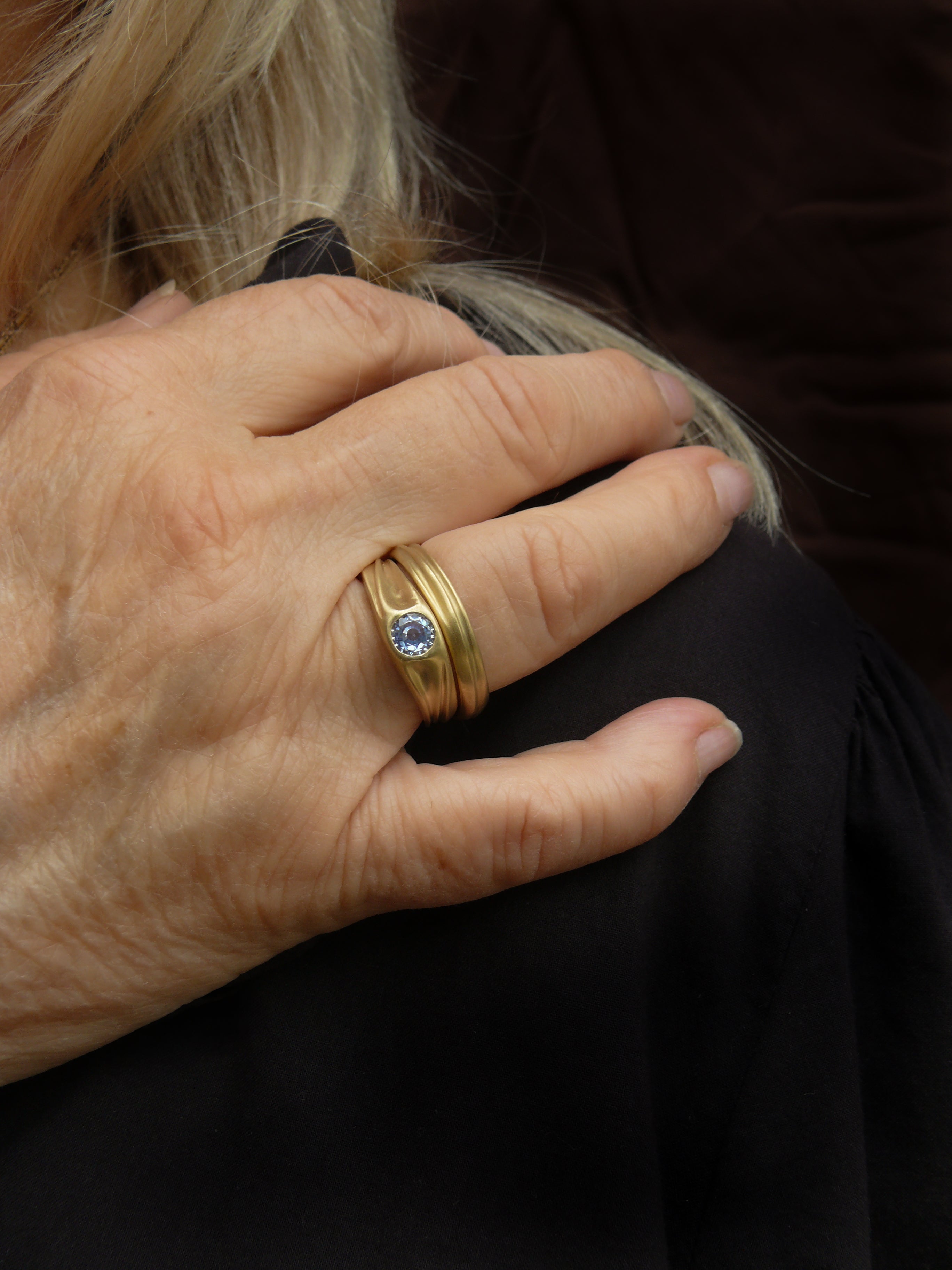 Hand wearing a gold organic dune rings with a blue sapphire on a dark background