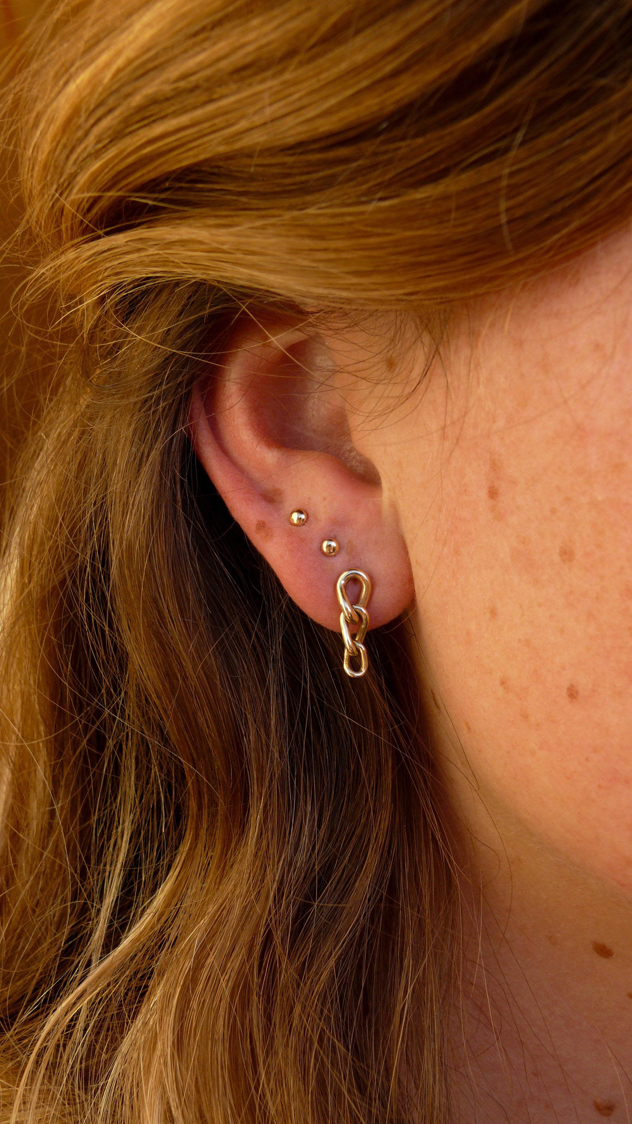 Gold short curb chain earrings stacked on ear with two gold grain studs