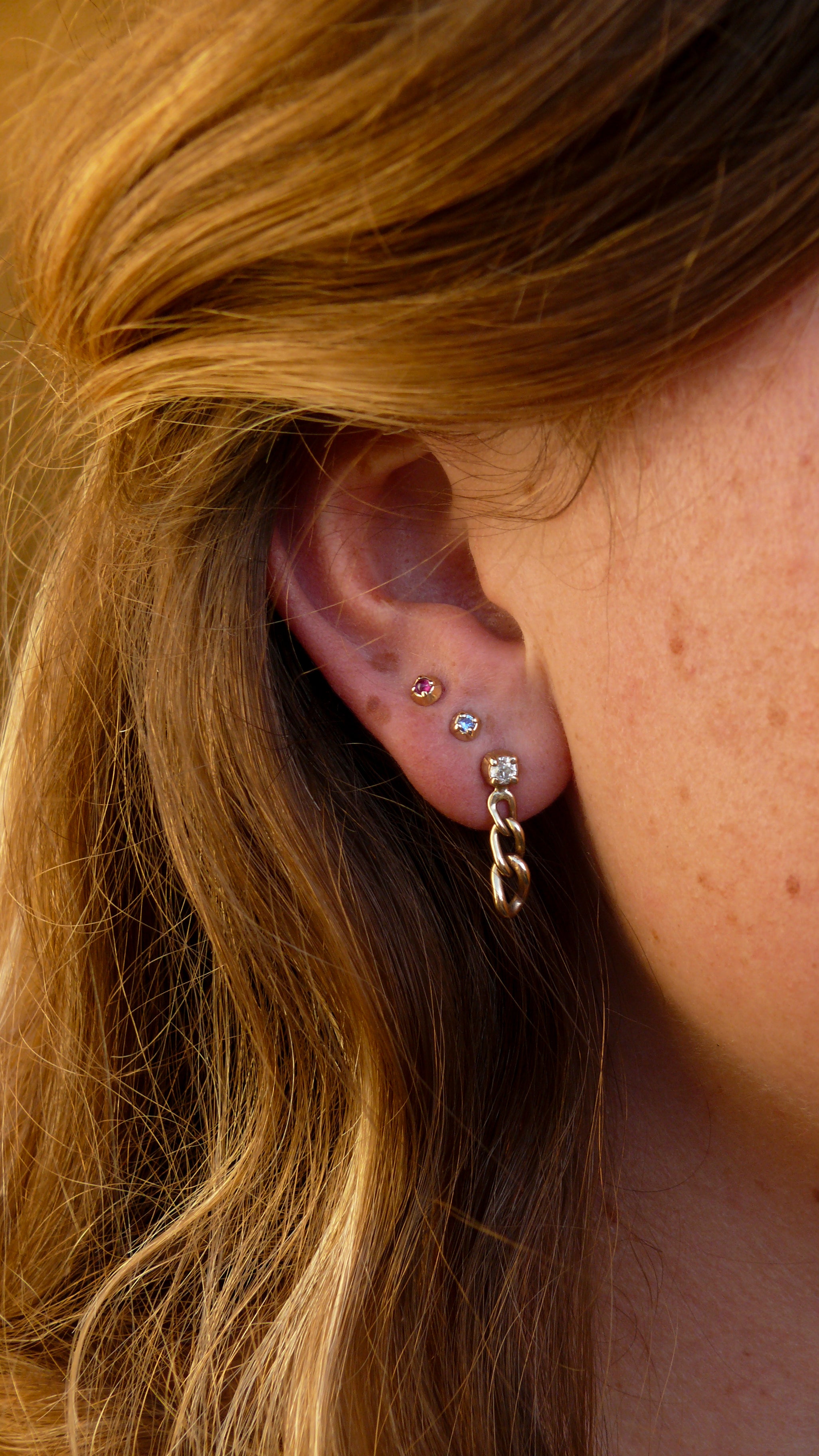 Gold short curb chain earrings stacked on an ear with gold sapphire and ruby stud earring