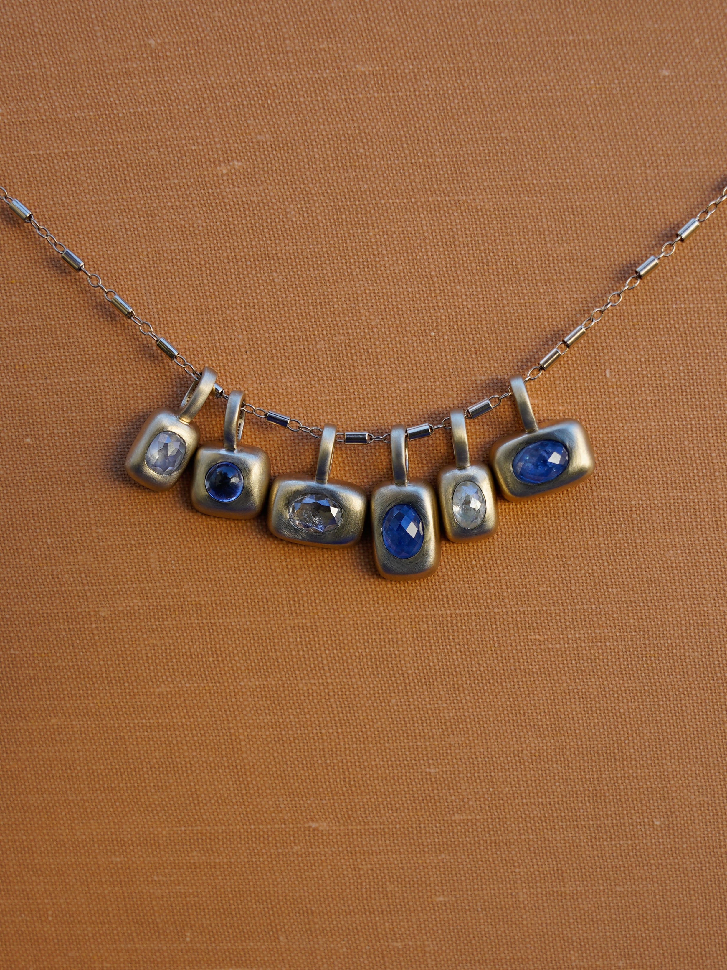 Diamond and Sapphire Trove charms on stellar bar chain on mustard yellow linen background