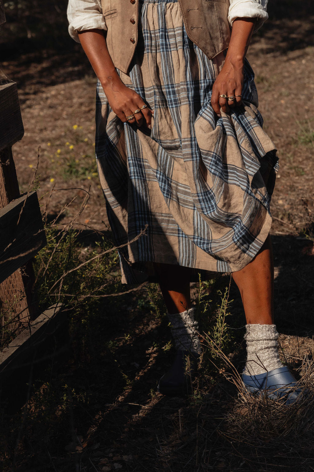 Person wearing a plaid skirt and gold trove collection jewelry in a natural setting