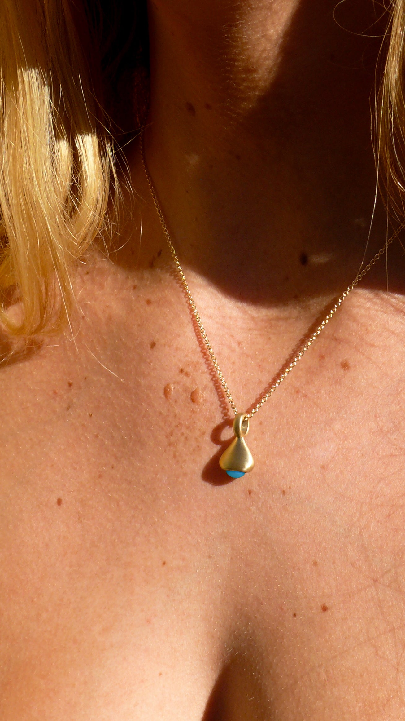 Gold pendulum charm no. 3 with turquoise on a person's neck