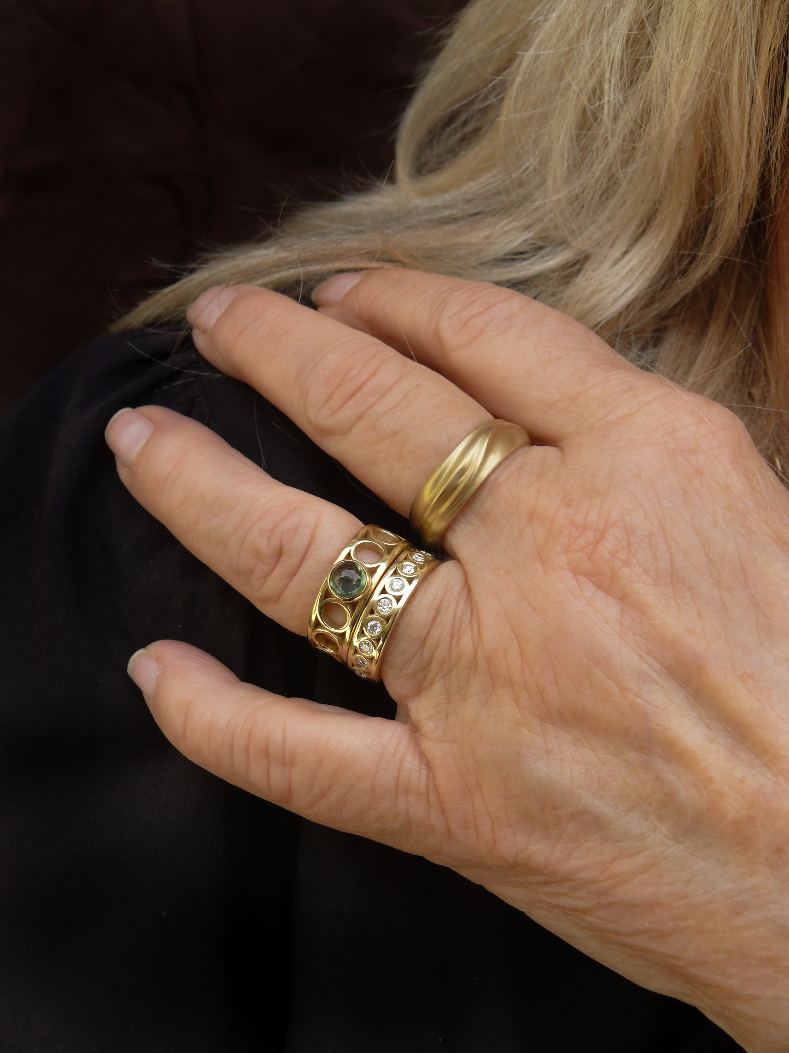 hand with gold wide dune ring and cylinder rings with sapphire and eternity diamonds on dark background