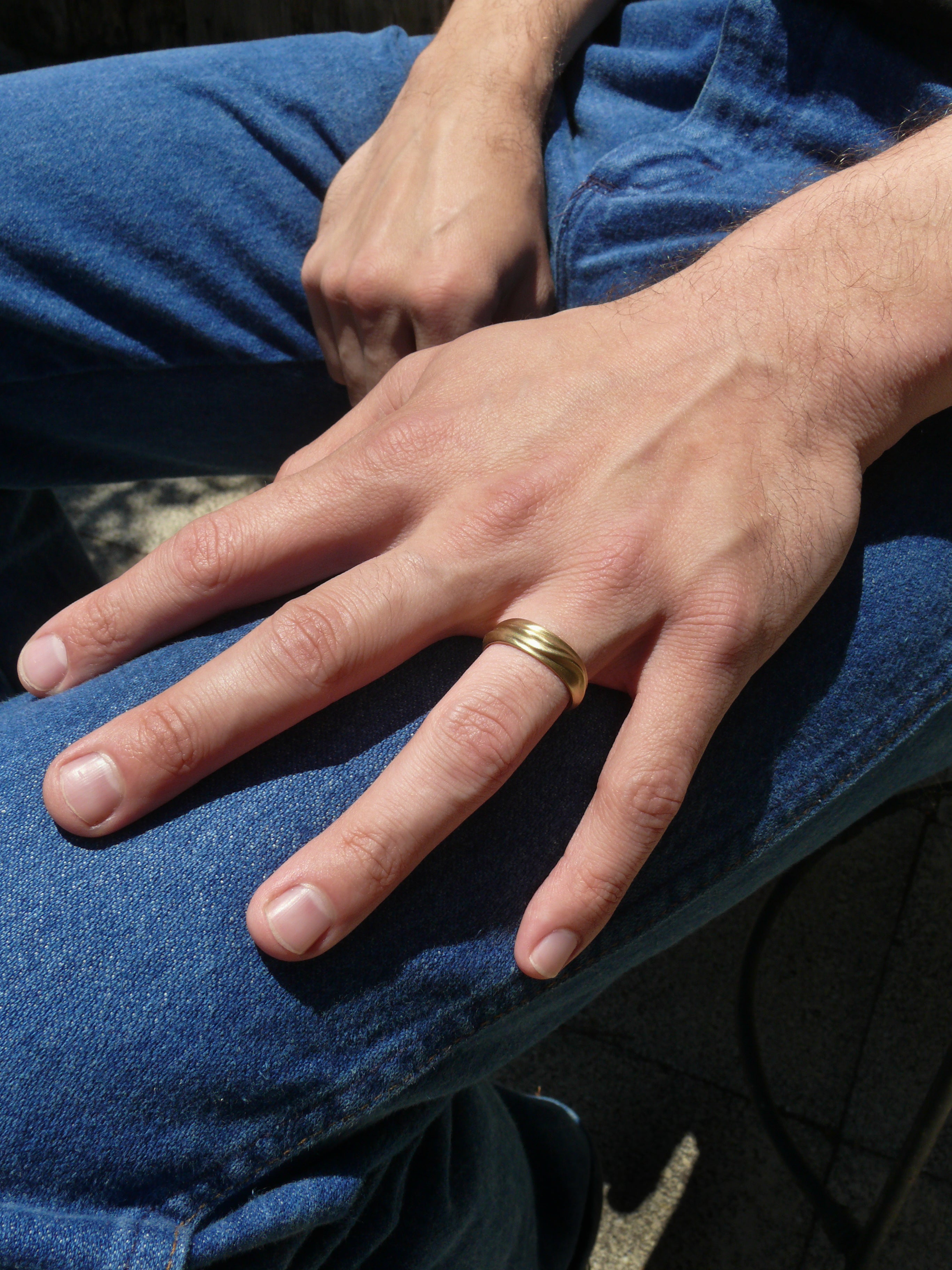 Hand wearing a gold wide dune ring on a blue denim background