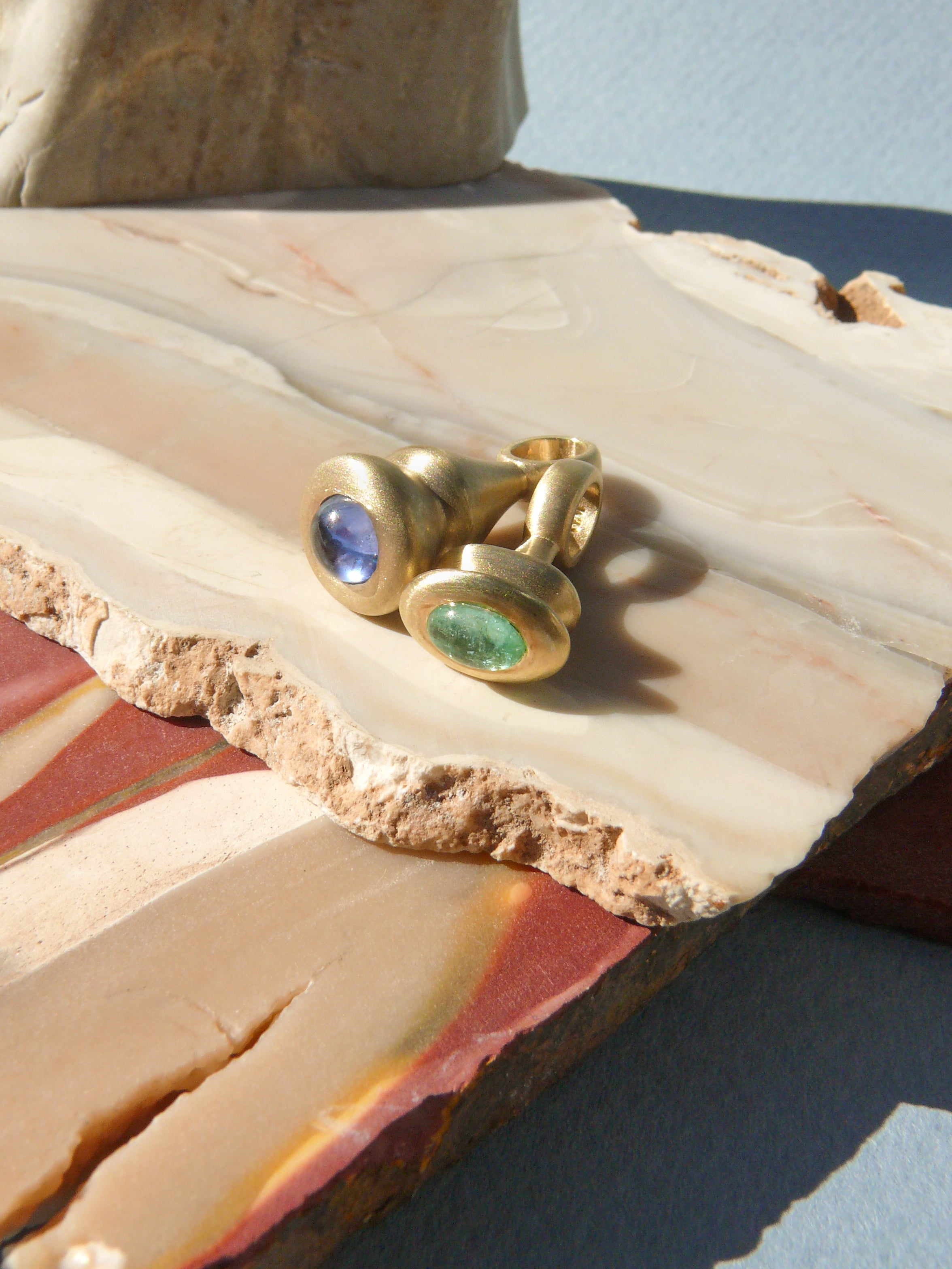 blue sapphire pendulum charm no. 1 and green beryl pendulum charm no. 9 on rough jasper background