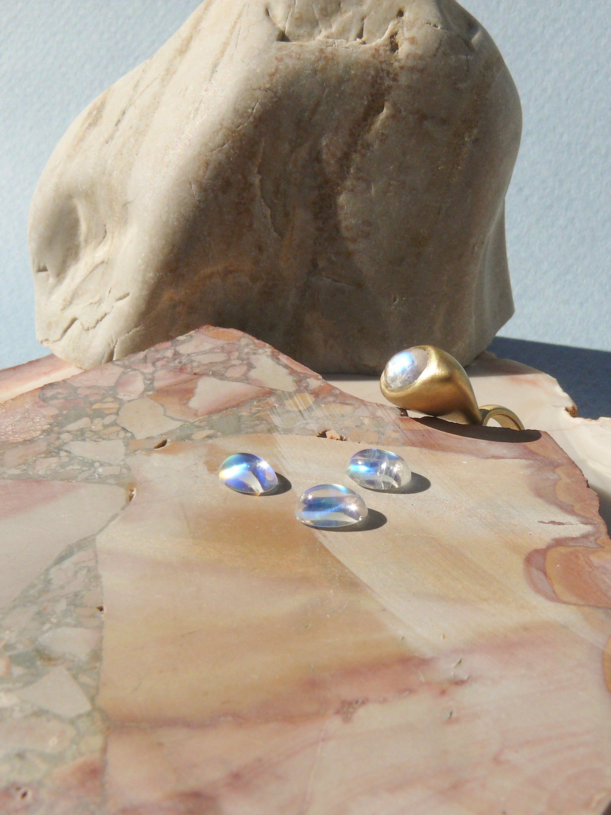 gold moonstone pendulum charm no. 3 with loose gemstones on rough jasper background