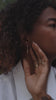 Model with curly hair wearing gold rings and pendulum charm hoop earrings with sapphires and emeralds, from the Made Line Jewelry Trove Collection. 